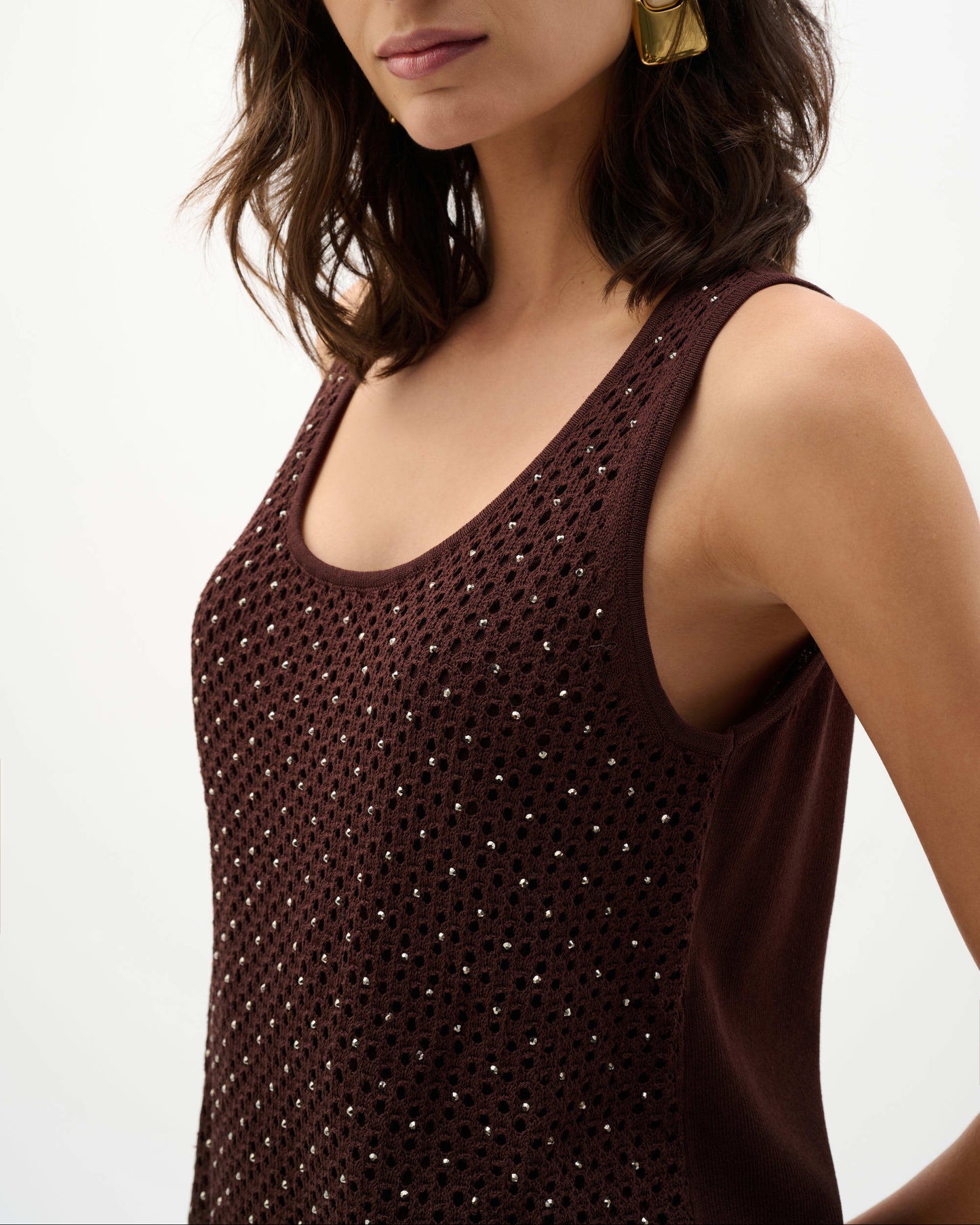 Woman wearing a brown sleeveless top with a textured pattern on a plain background