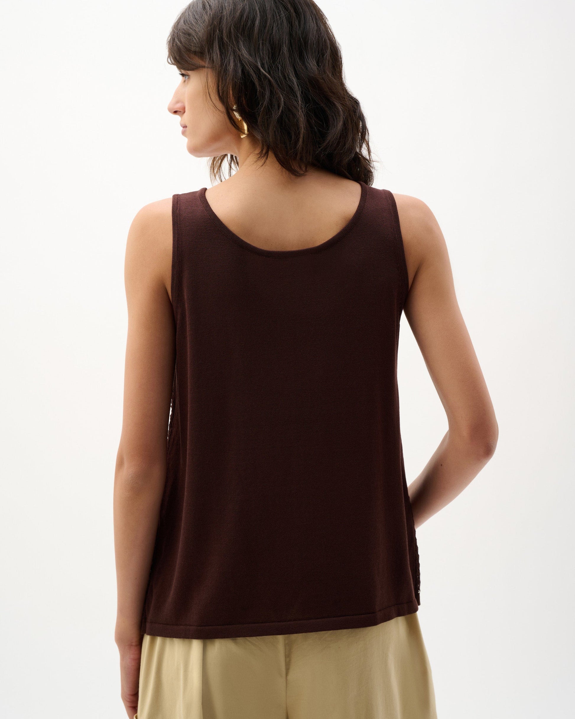 Woman wearing a brown sleeveless top and beige pants on a white background