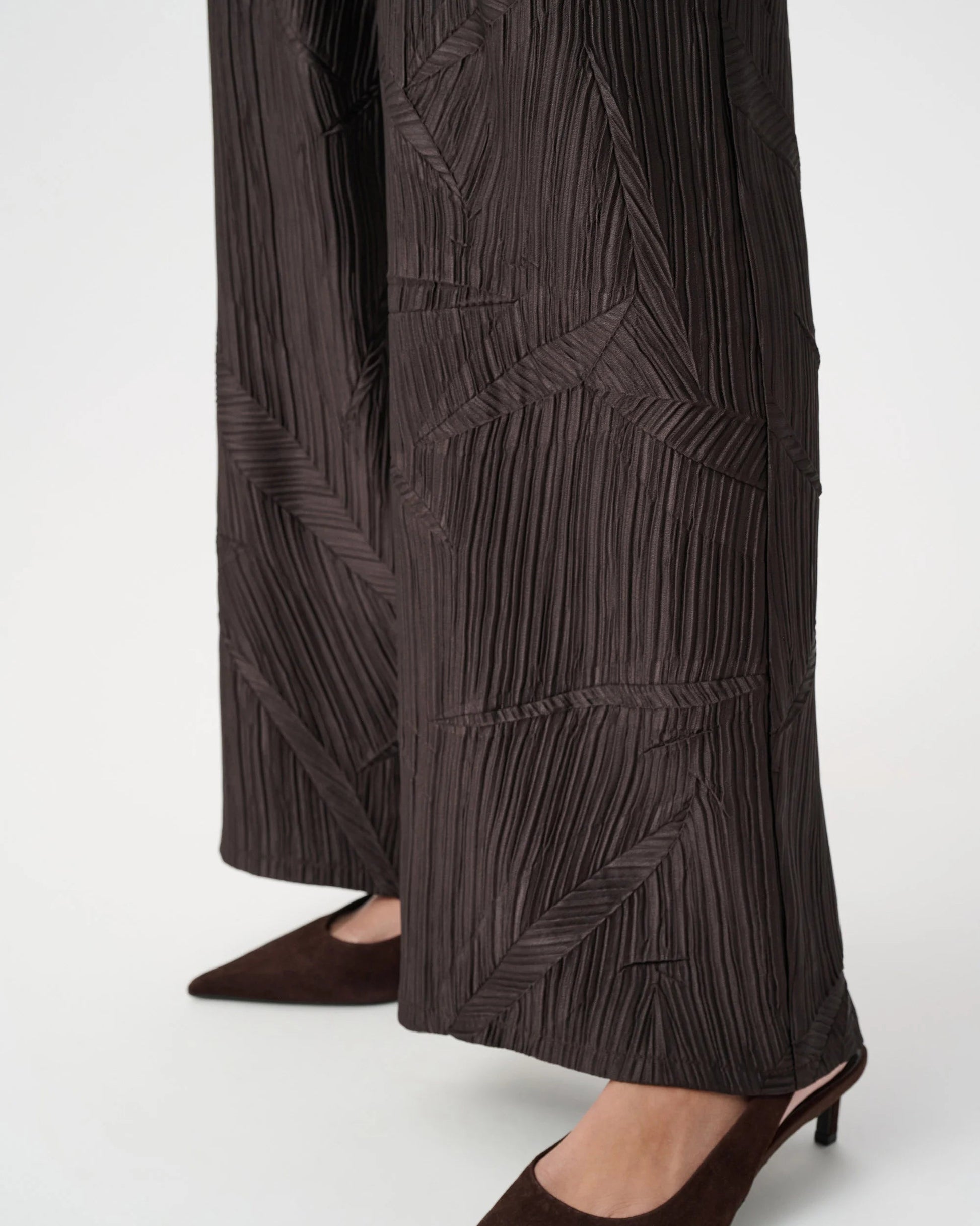 Dark brown pleated pants worn with brown shoes on a white background
