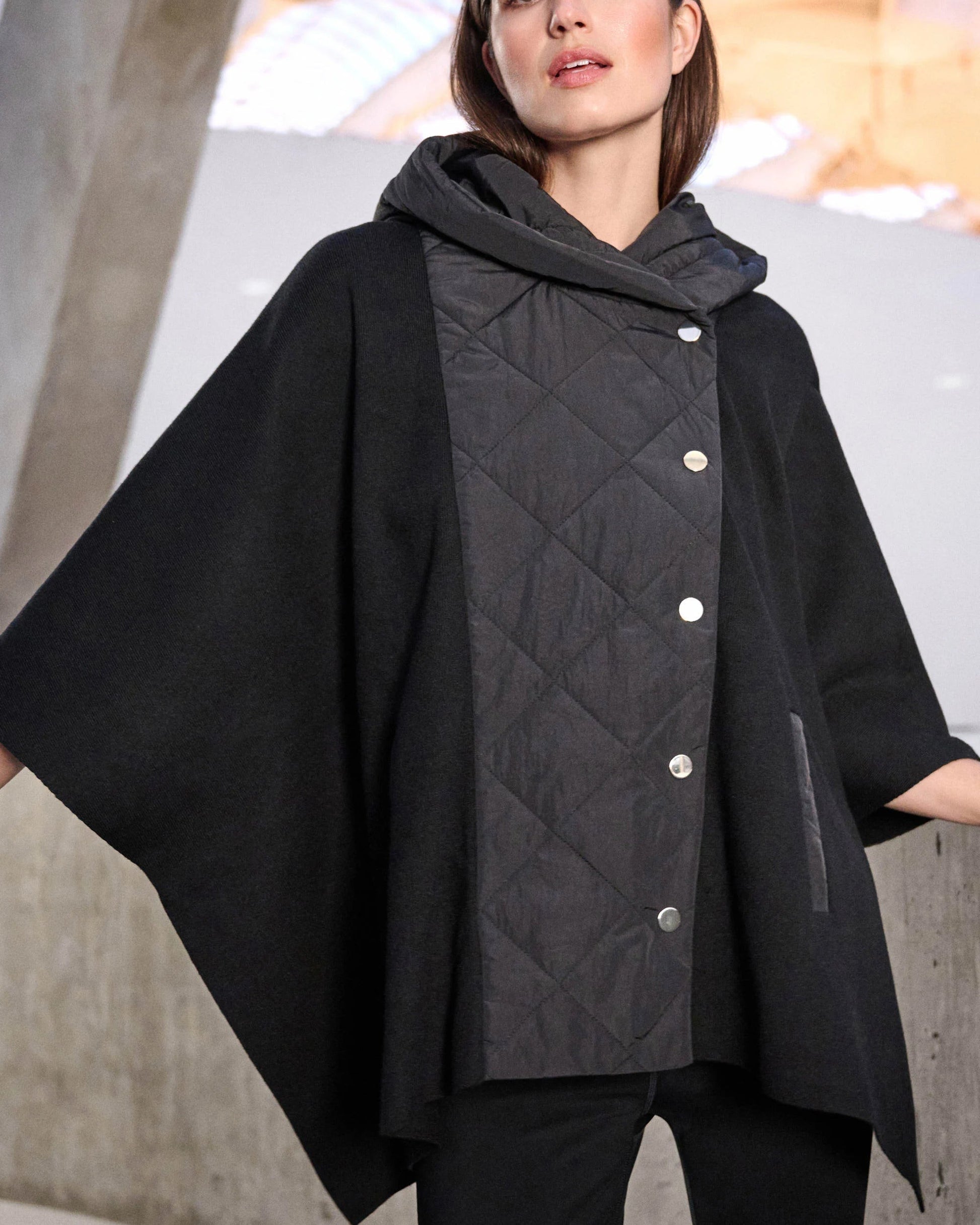 Woman wearing a black quilted jacket with a hood against a neutral background