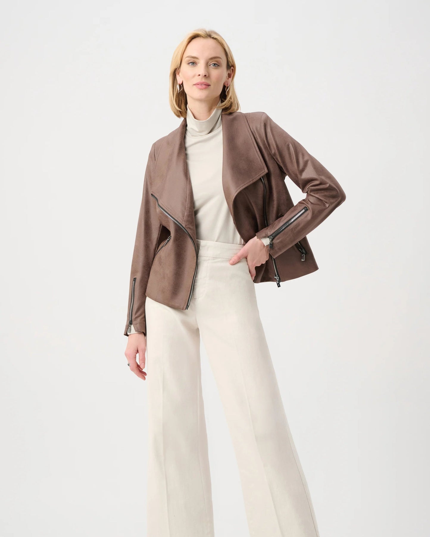Woman wearing a brown jacket, white turtleneck, and cream pants on a white background