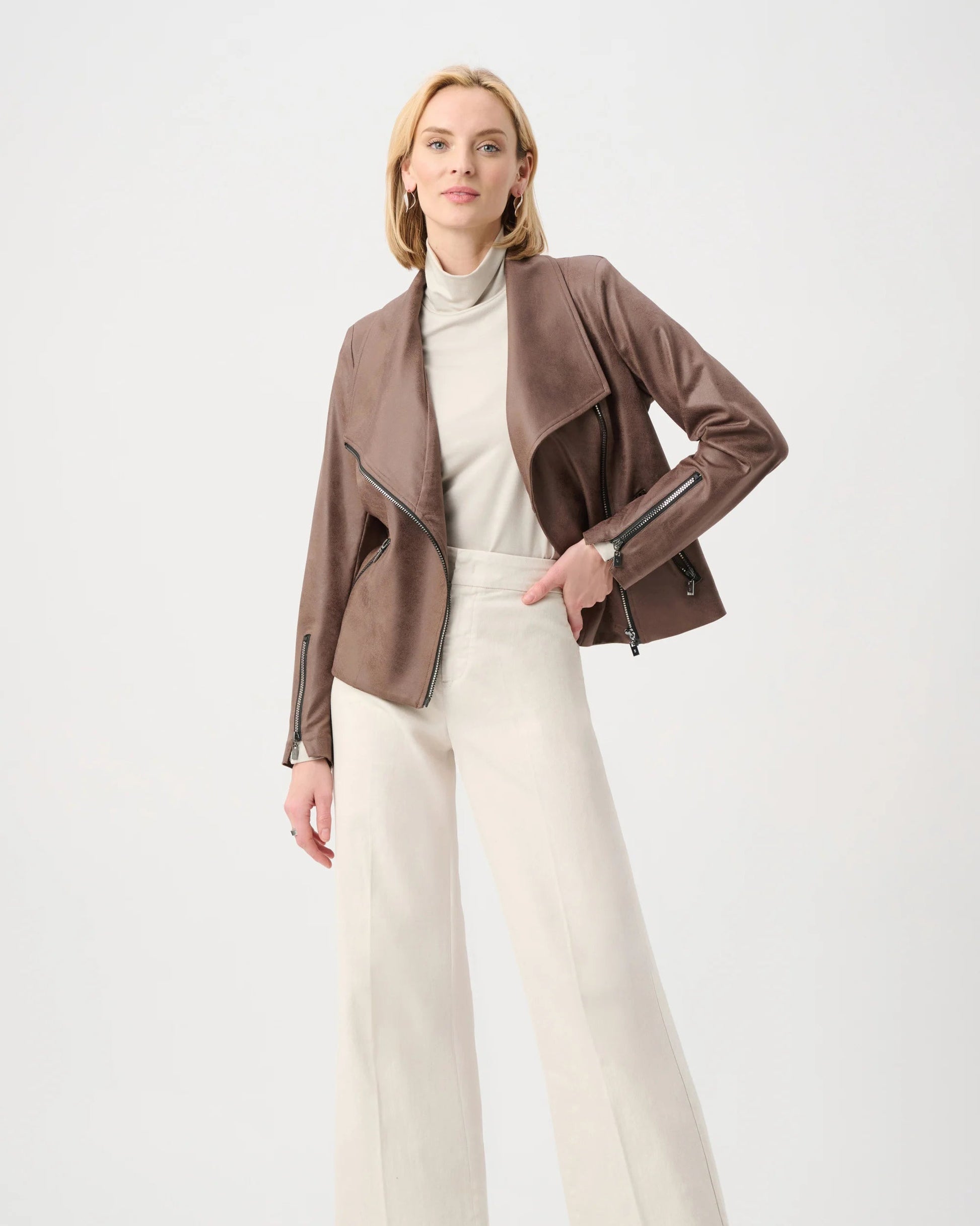 Woman wearing a brown jacket, white turtleneck, and cream pants on a white background