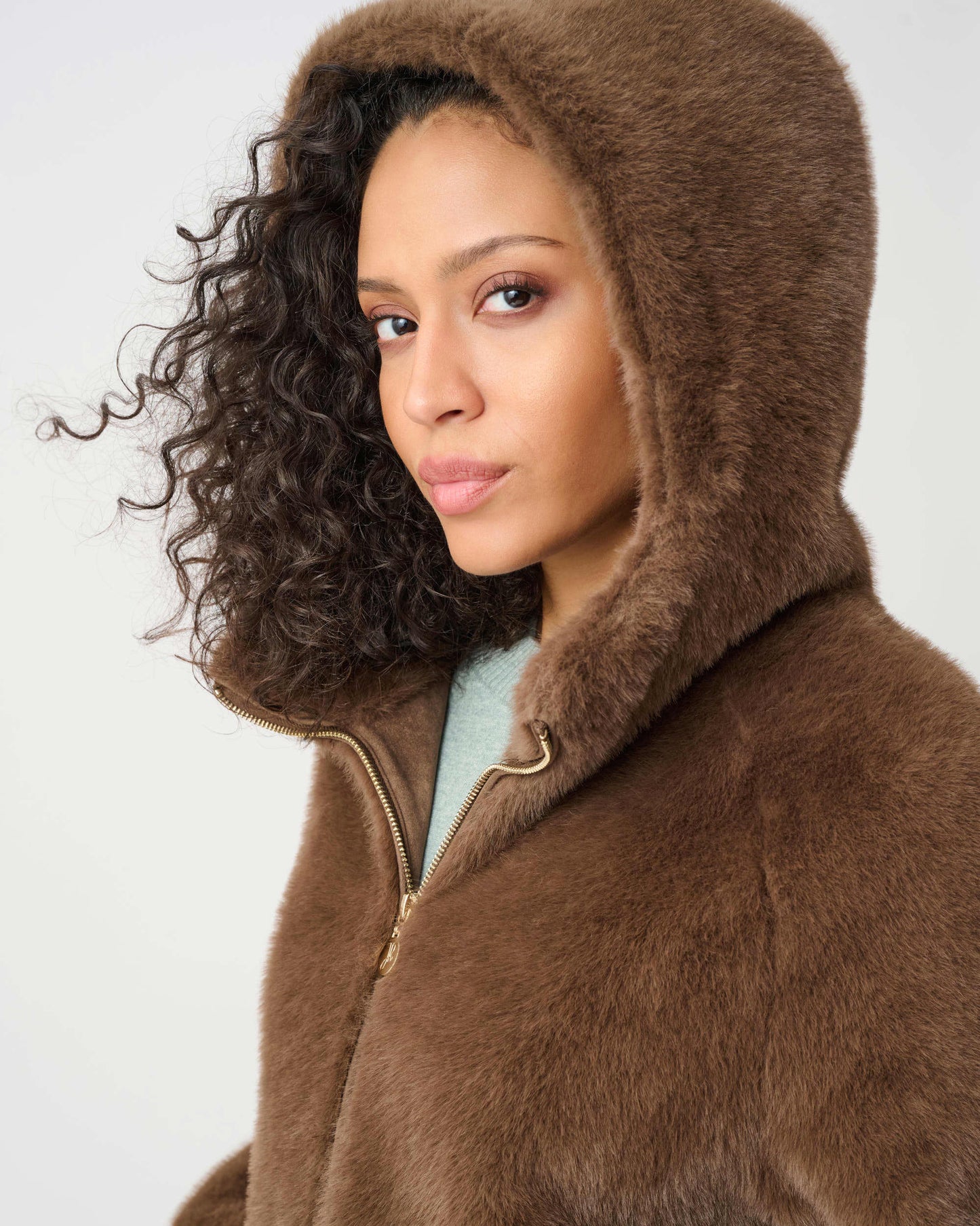 Woman wearing a brown fur coat with a hood on a white background