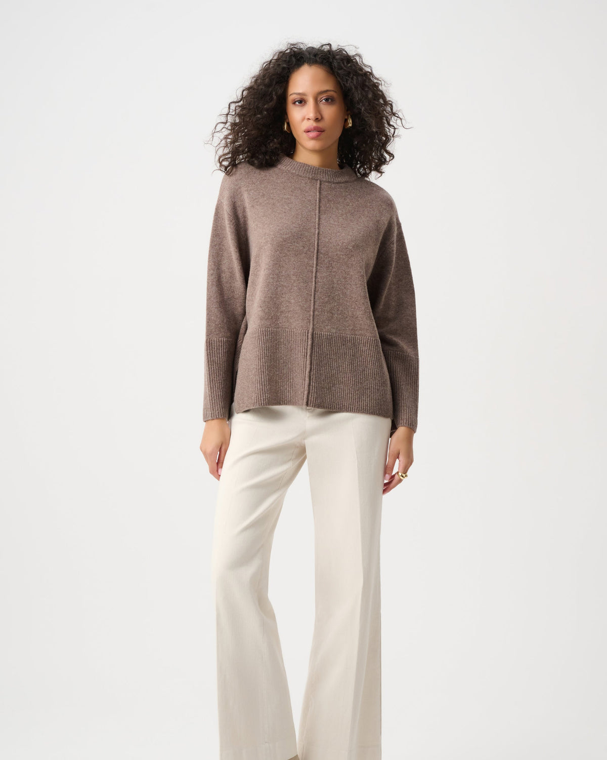 Woman wearing a brown sweater and white pants on a white background