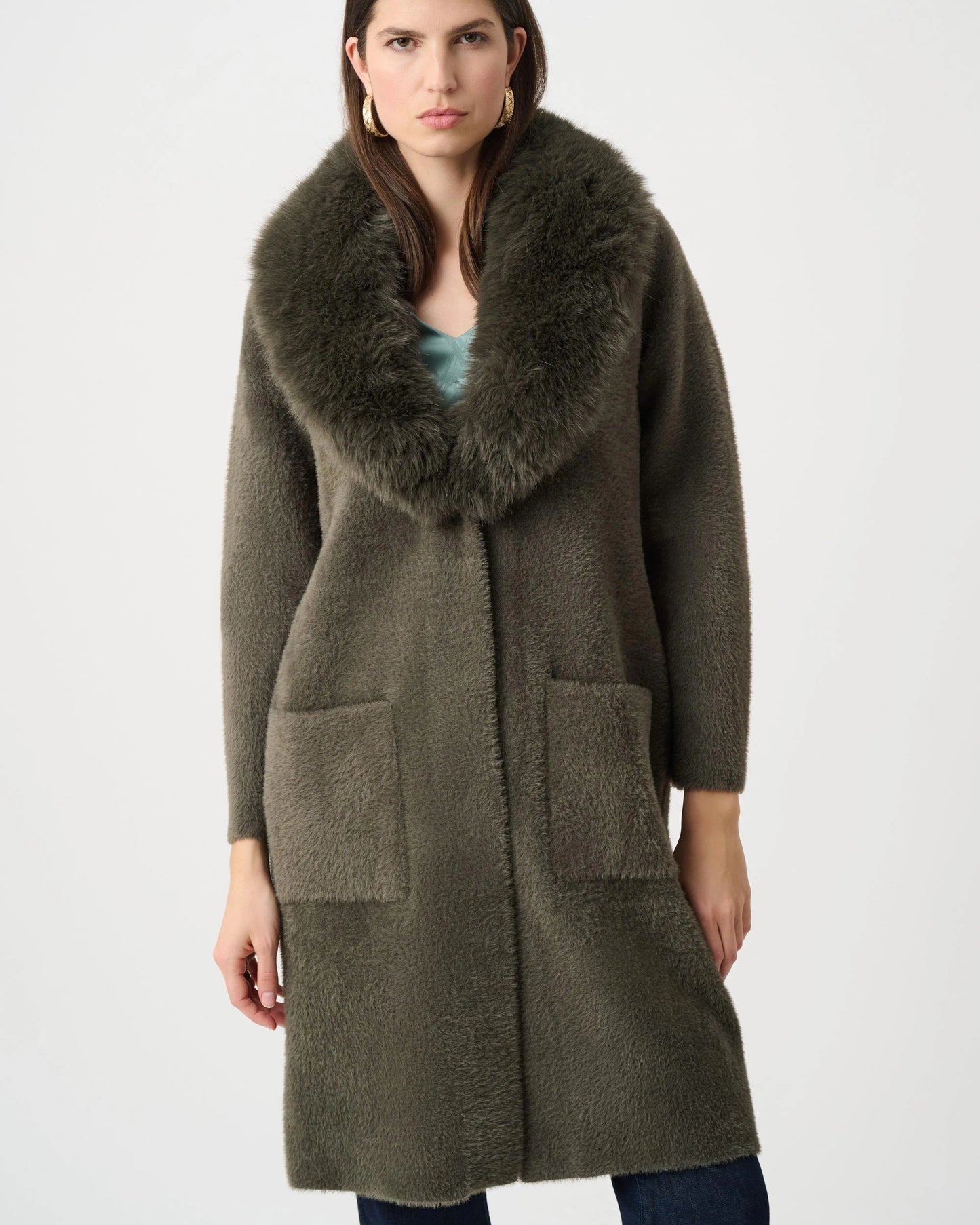 Woman wearing a long olive green coat with a fur collar on a white background
