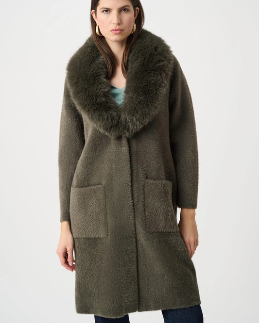 Woman wearing a long olive green coat with a fur collar on a white background