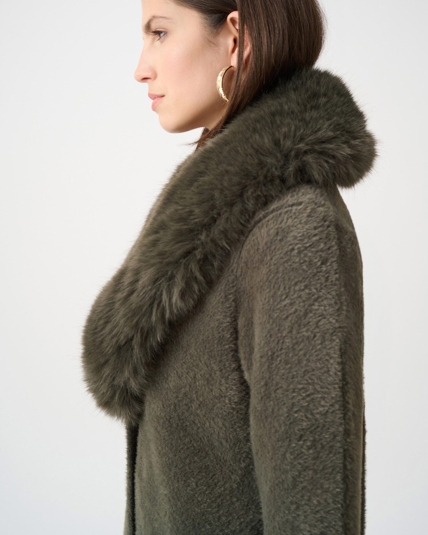 Woman wearing a dark green coat with a fur collar against a white background