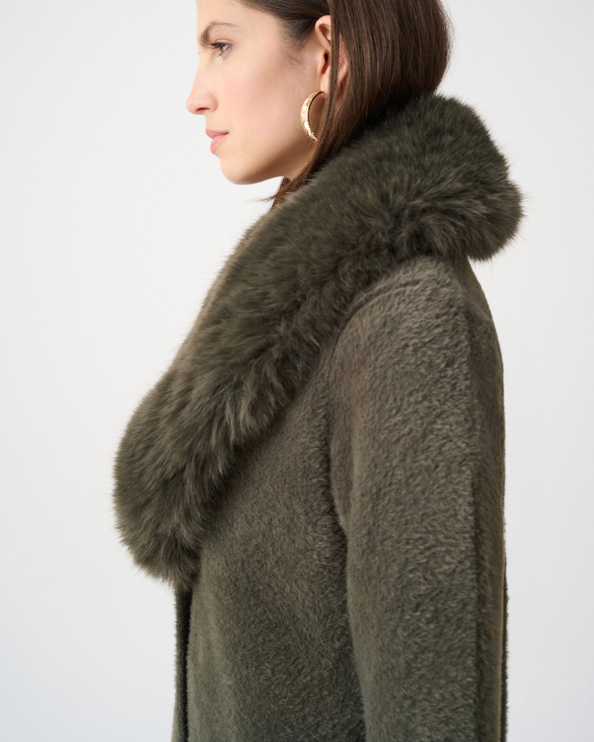 Woman wearing a dark green coat with a fur collar against a white background