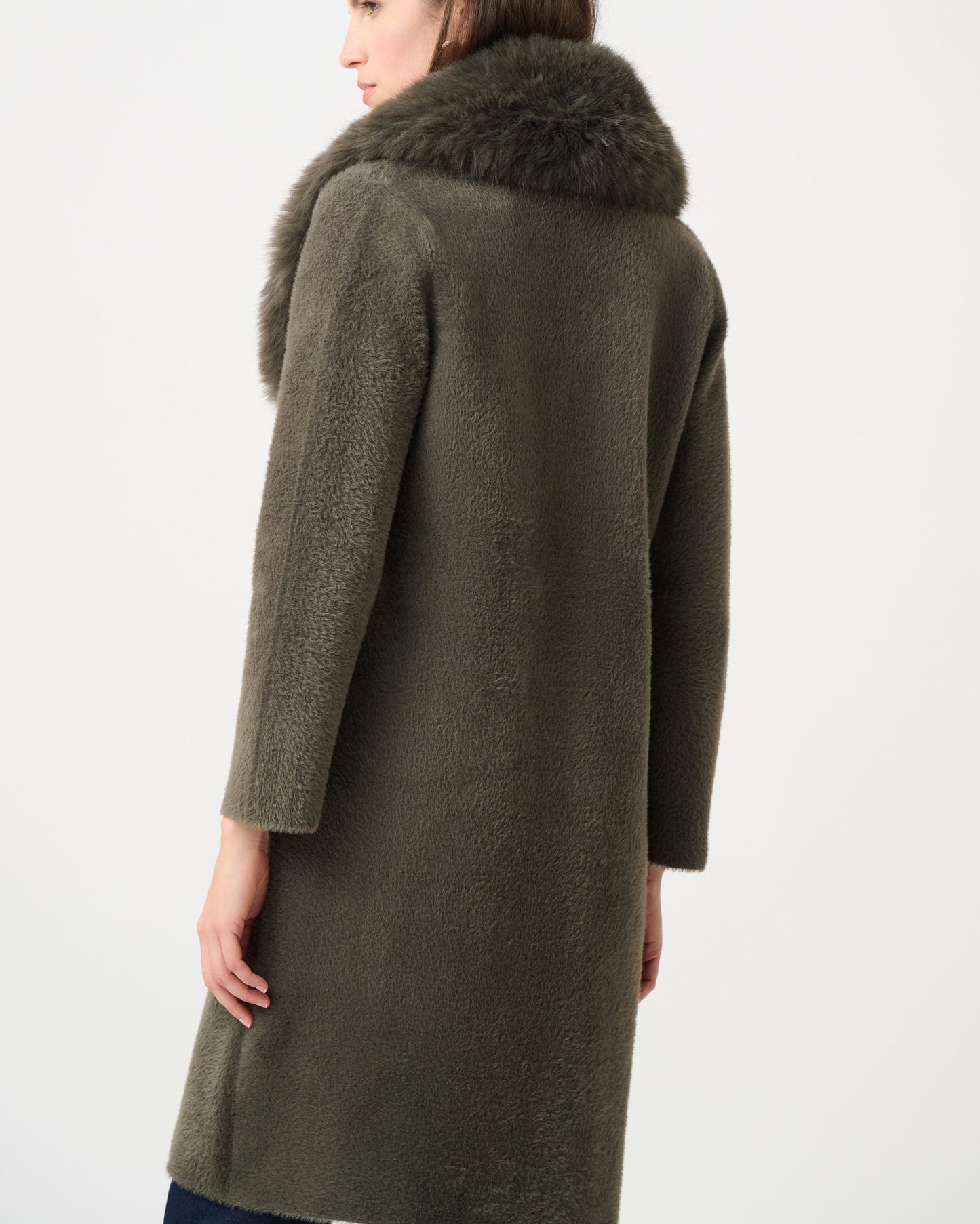 Woman wearing a long olive green coat with fur collar on a white background