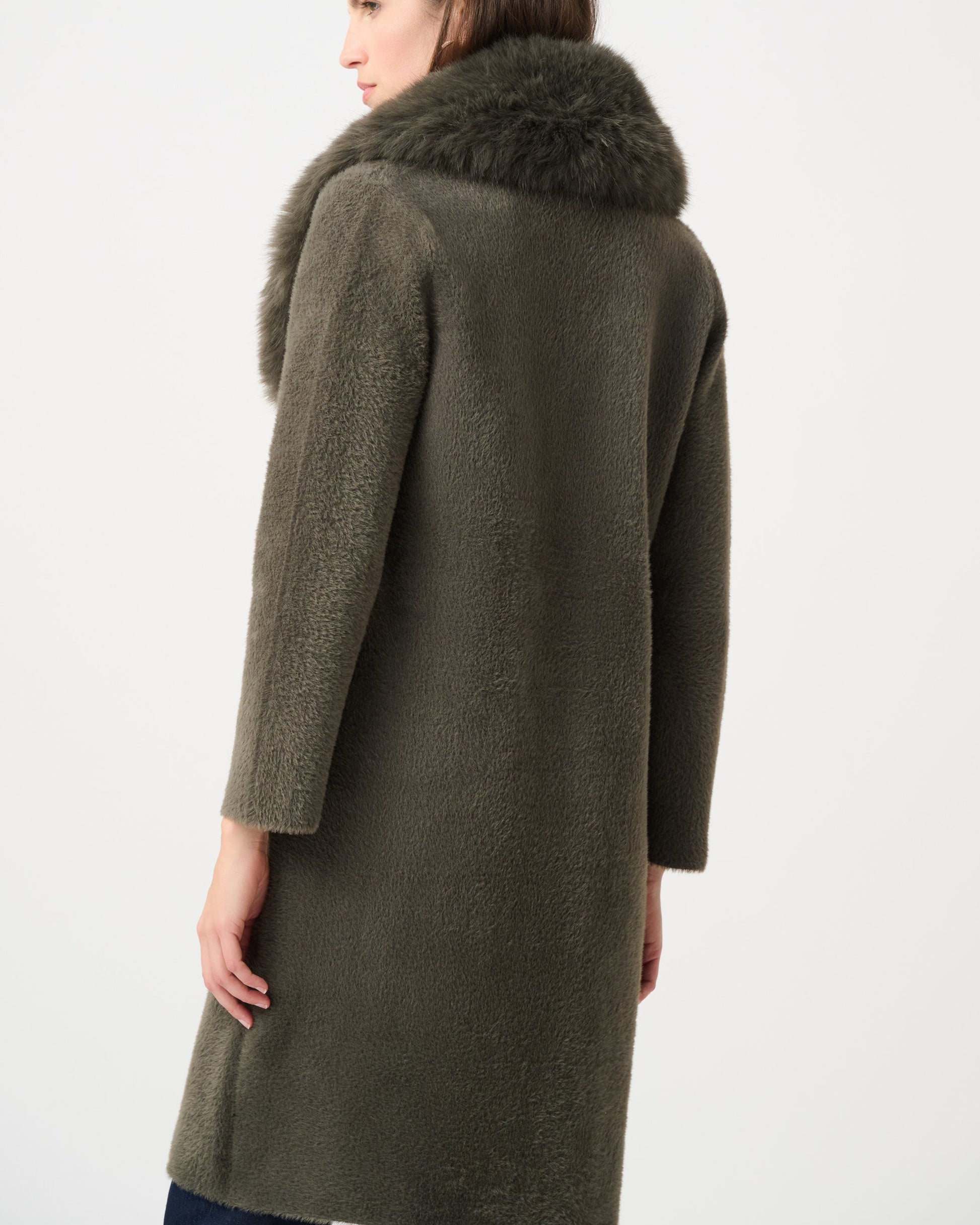 Woman wearing a long olive green coat with fur collar on a white background