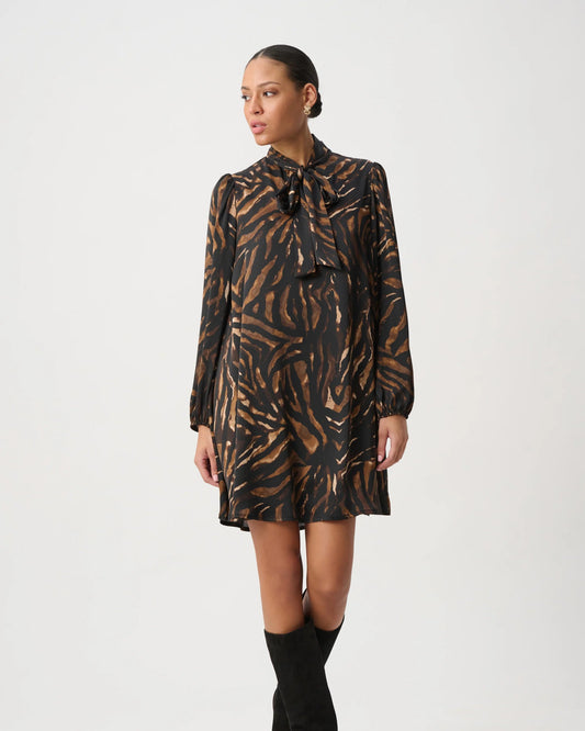 A model wearing a long-sleeved mini dress with a brown and black tiger-stripe pattern, paired with black knee-high boots, against a plain light gray studio background.