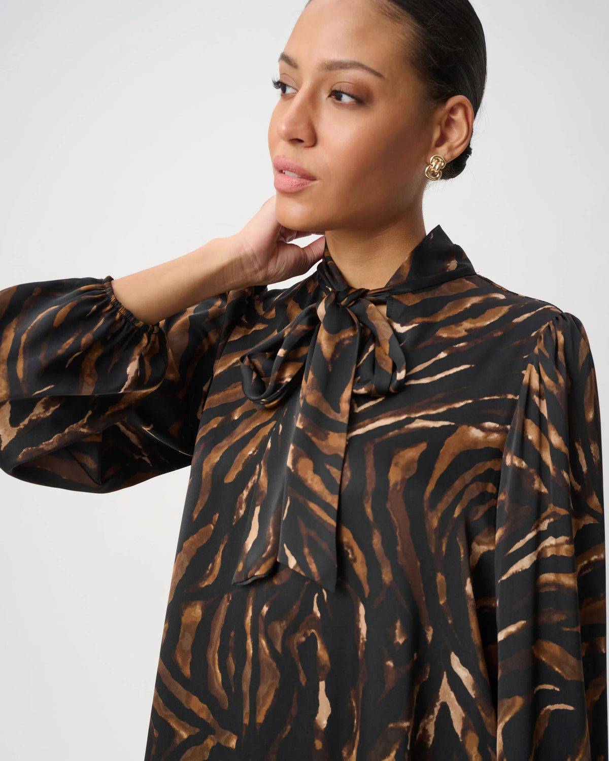 A woman wearing a black and brown zebra-print blouse with a high neck and bow tie collar, photographed against a light gray studio background.