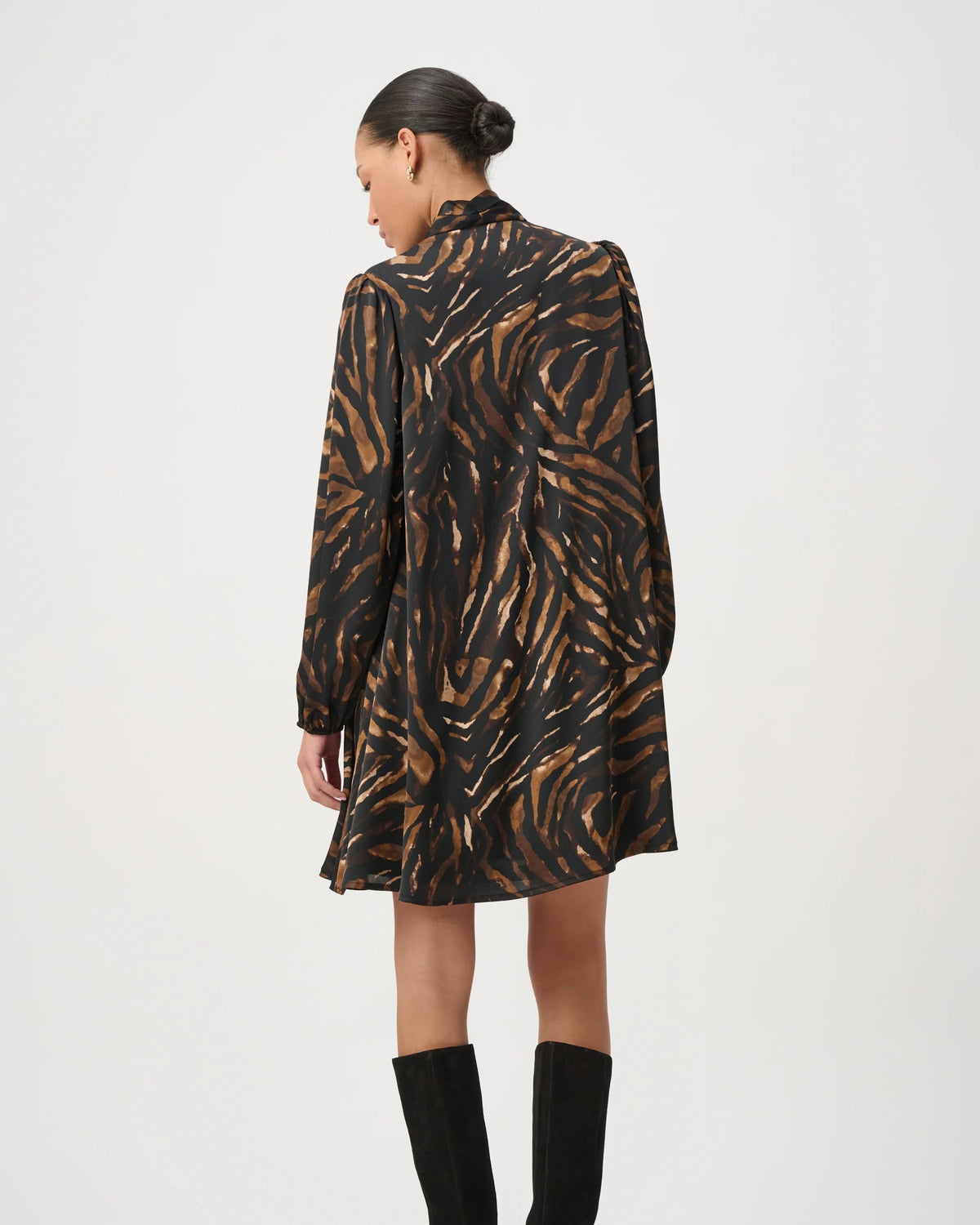A model is shown from the back wearing a black and brown abstract patterned long-sleeve dress with black over-the-knee boots, set against a plain light gray studio background.