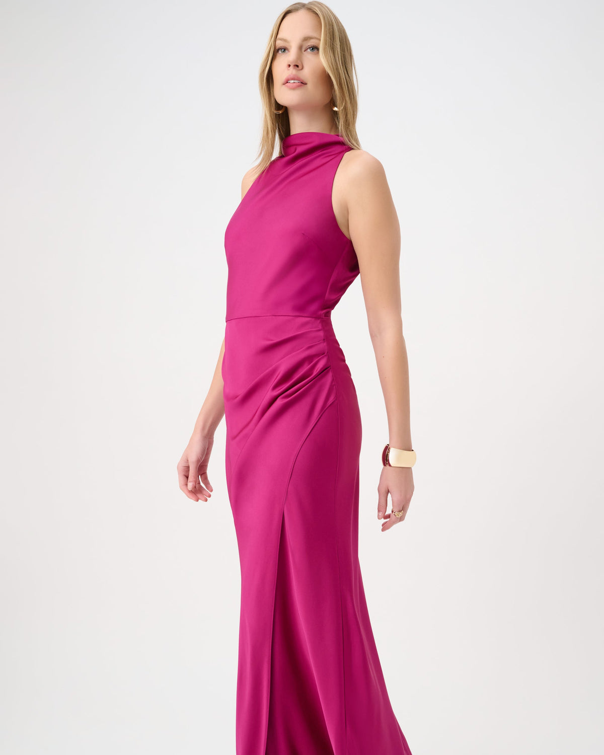 A woman modeling a sleeveless, high-neck, floor-length magenta gown against a plain light gray studio background.