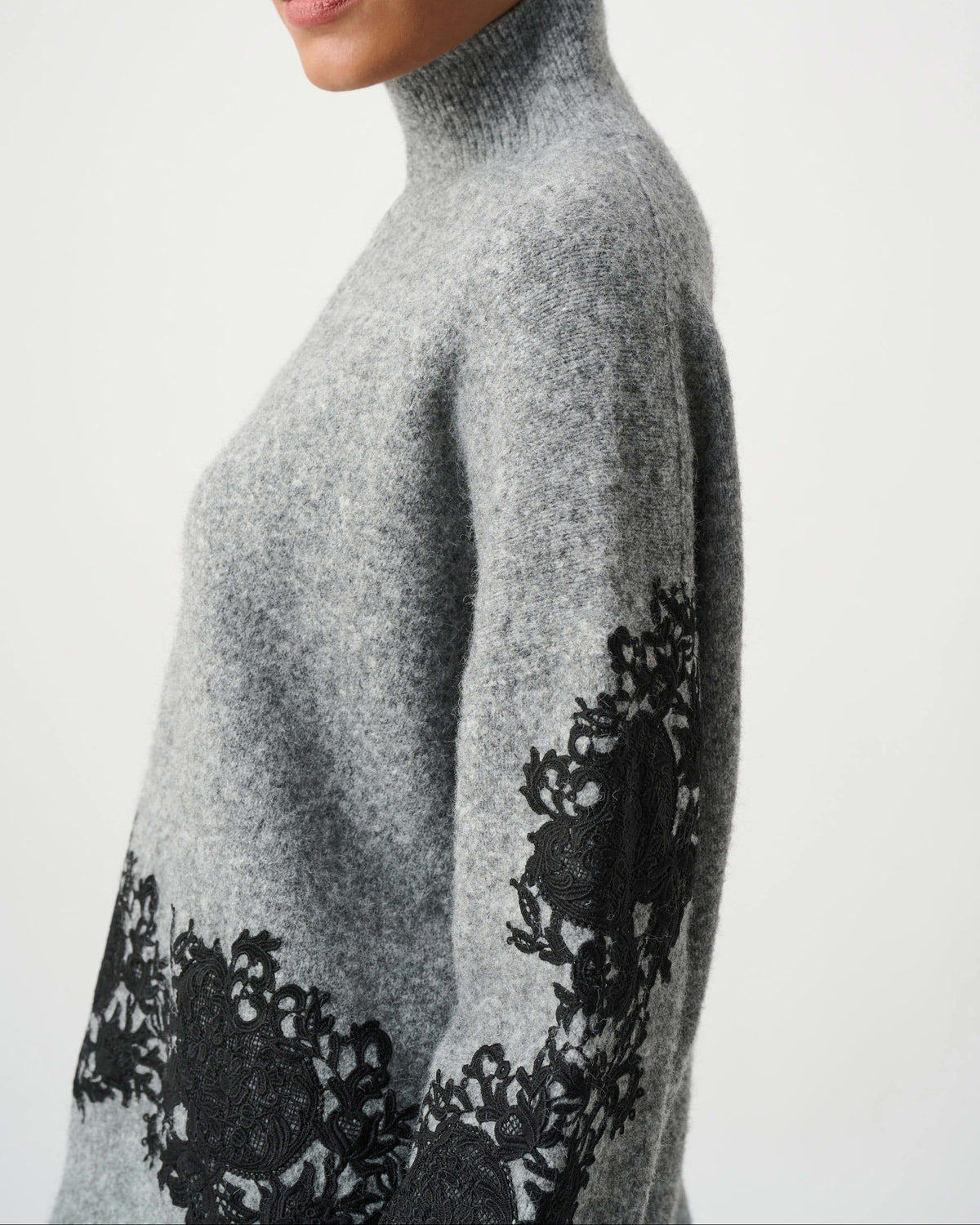 Woman wearing a gray turtleneck sweater with black floral patterns on the sleeves against a white background