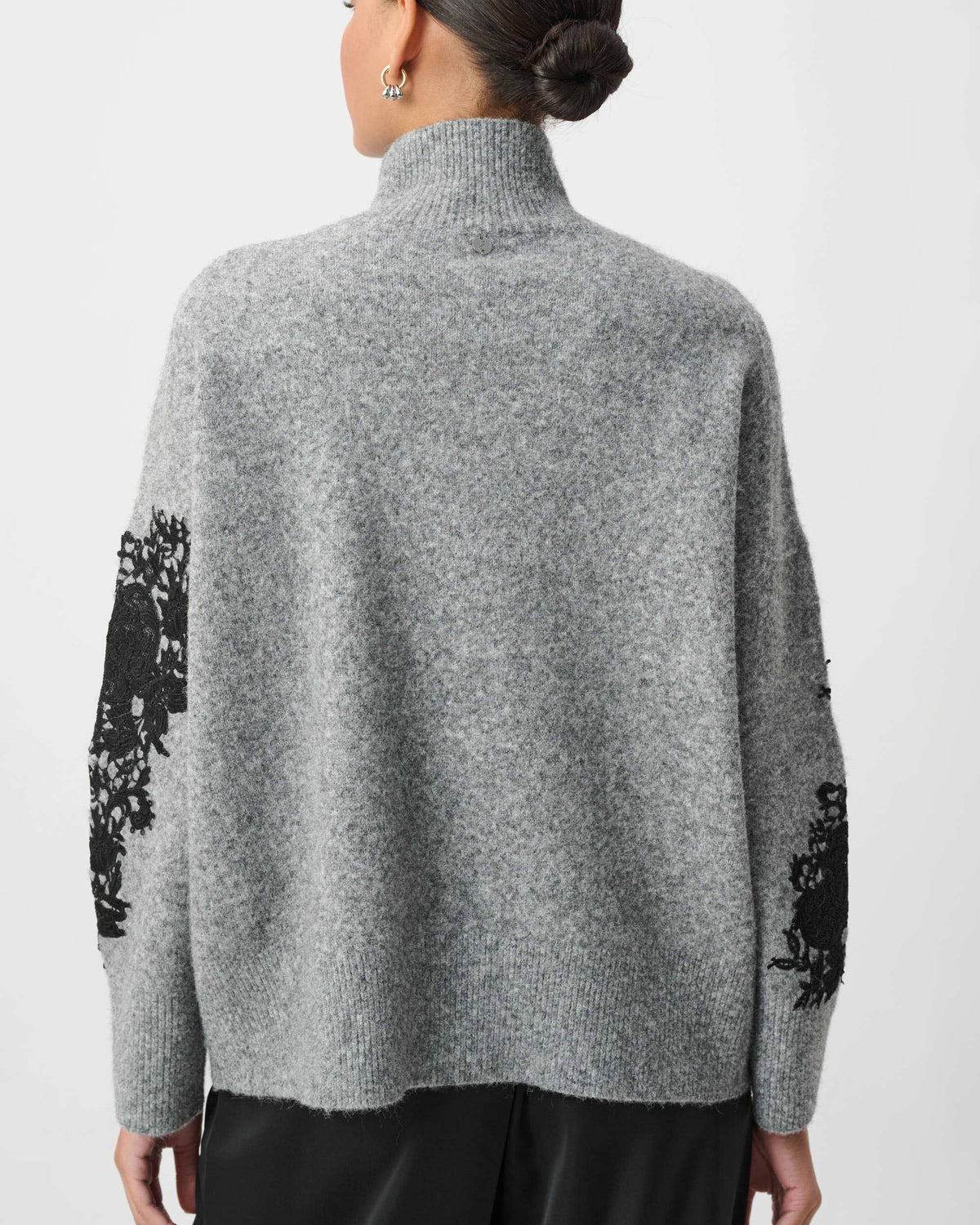 Person wearing a gray sweater with black floral patterns on sleeves against a white background