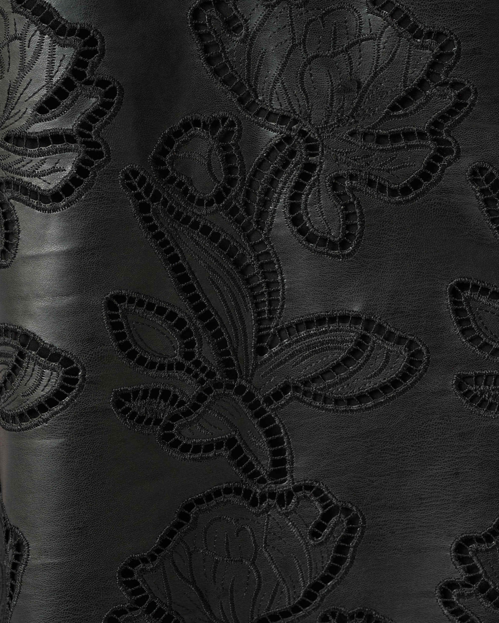 Close-up of a black fabric surface with an embossed or tonal floral pattern, showing the texture and sheen of the material.