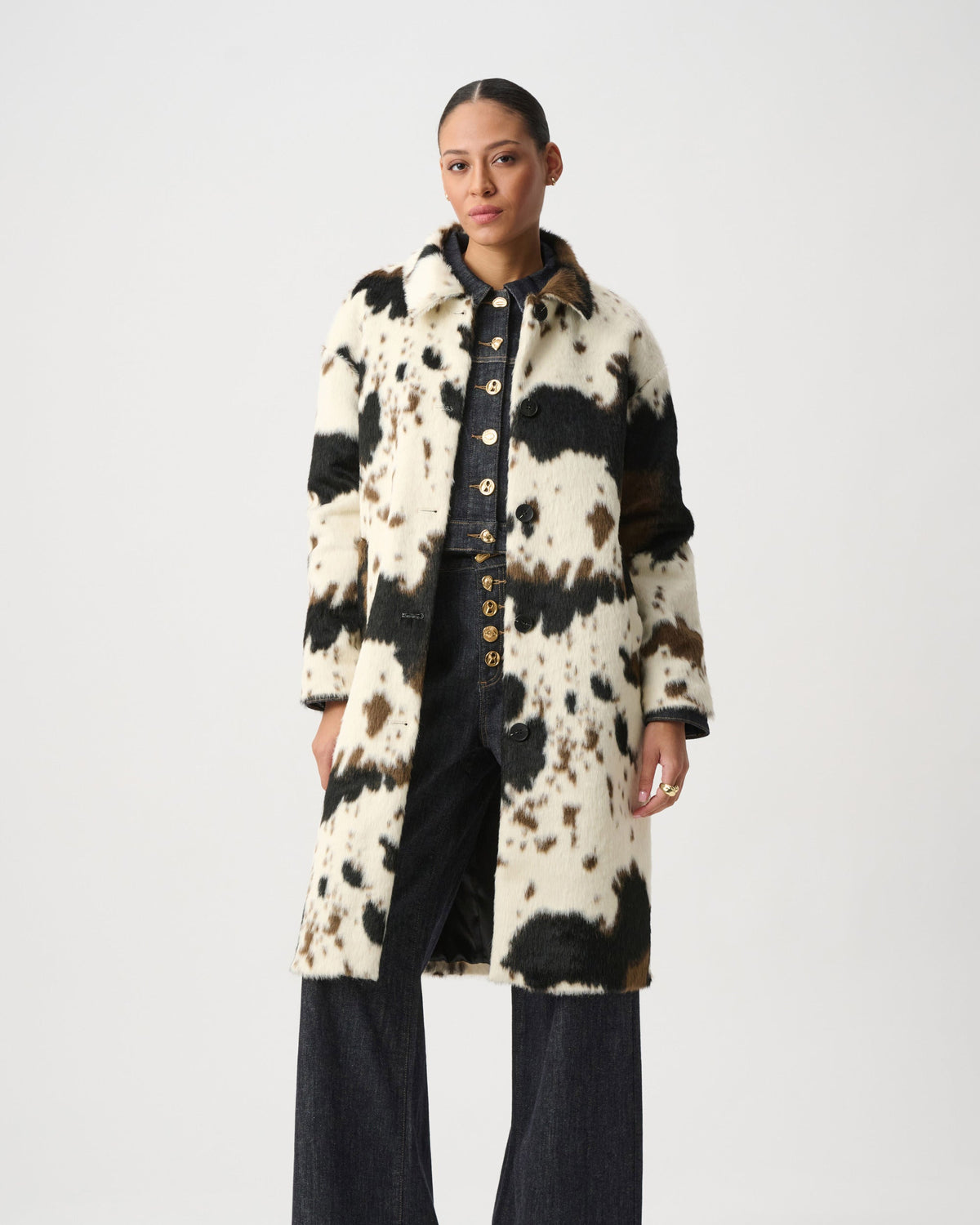 Model wearing a cow print long coat over dark denim in front of a white background.