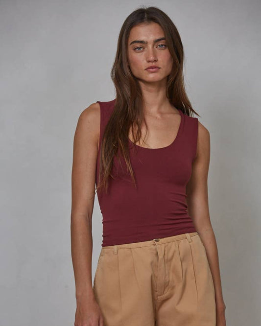 Woman wearing a maroon tank top and beige shorts against a gray background
