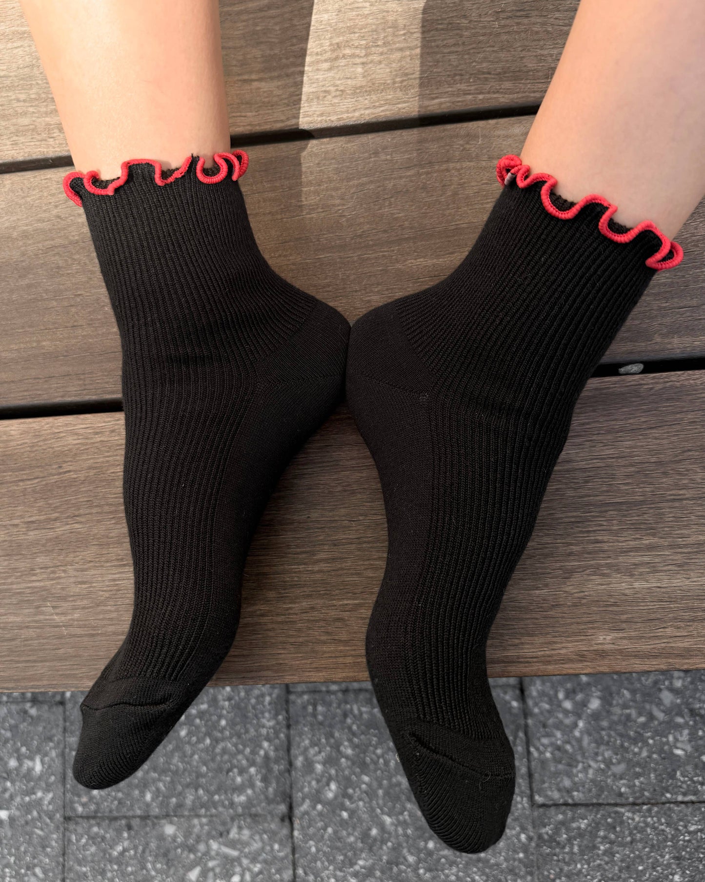 Black socks with red trim worn by a person sitting on wooden steps.