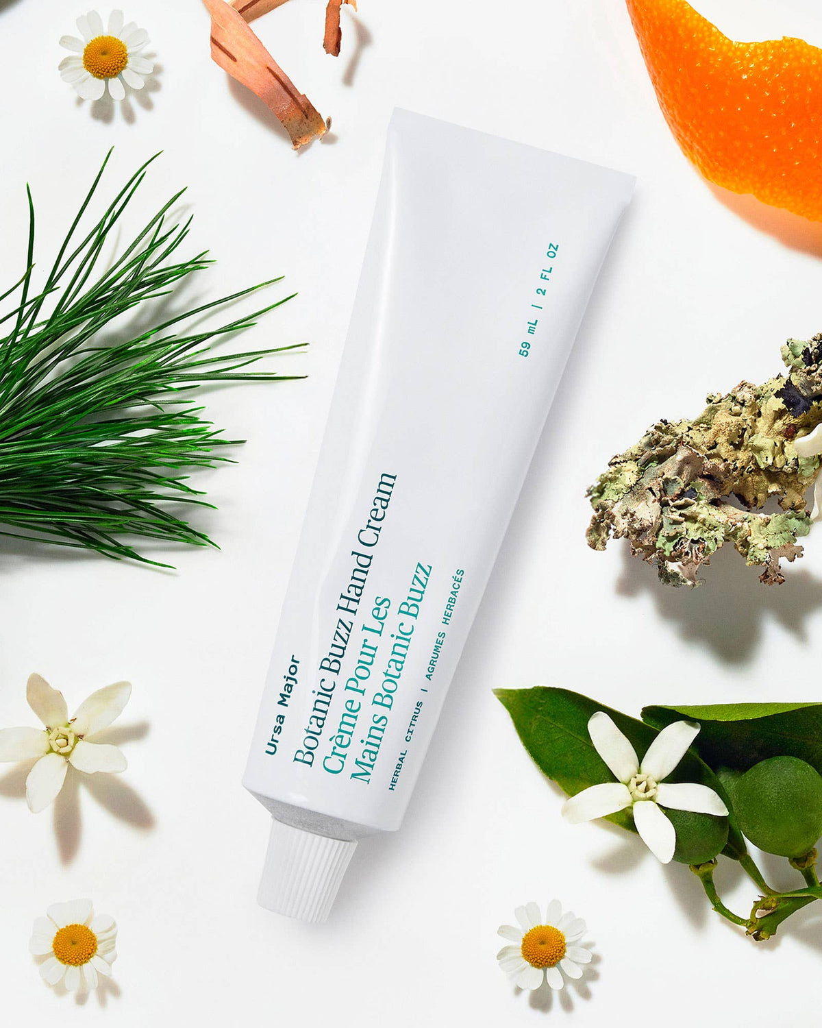 Hand cream tube labeled 'Ursa Major' surrounded by greenery and flowers on a white background