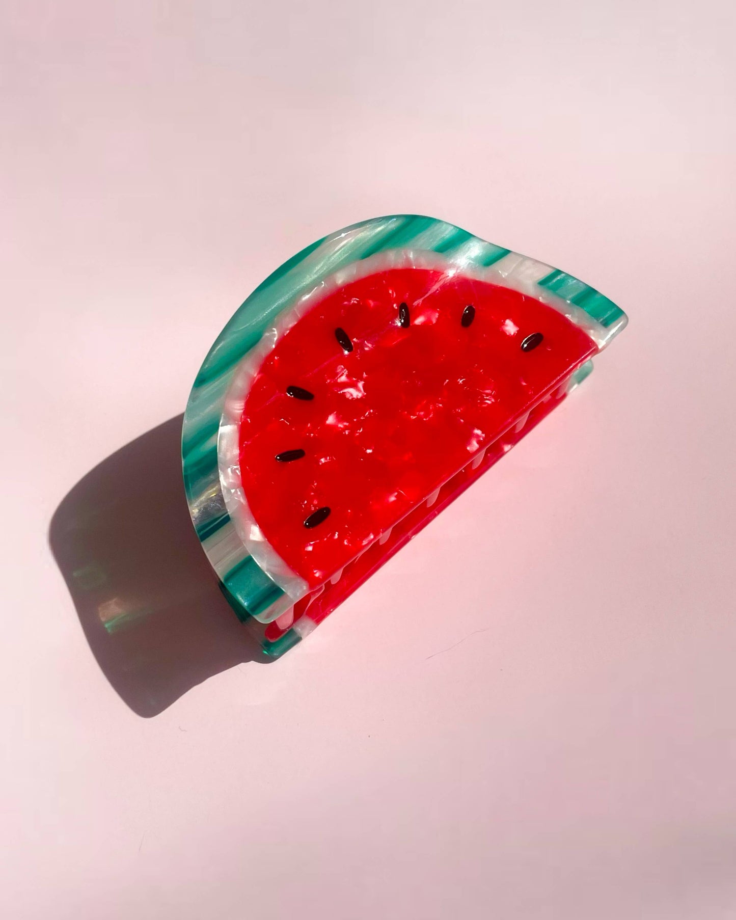 Red and green watermelon-shaped hair clip laying on a pink background
