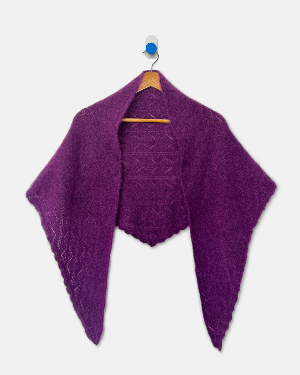 A purple textured knit shawl or capelet draped over a wooden hanger against a light gray background.