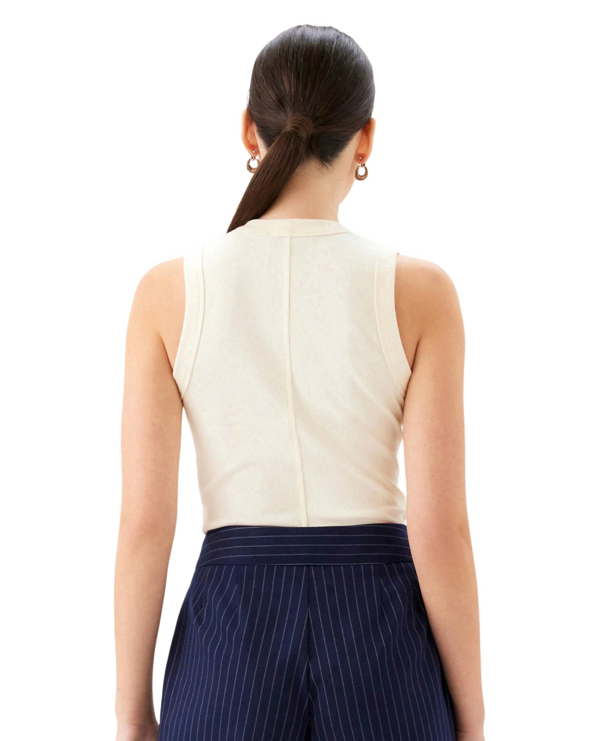 Woman wearing a white sleeveless top and navy pinstripe pants on a white background