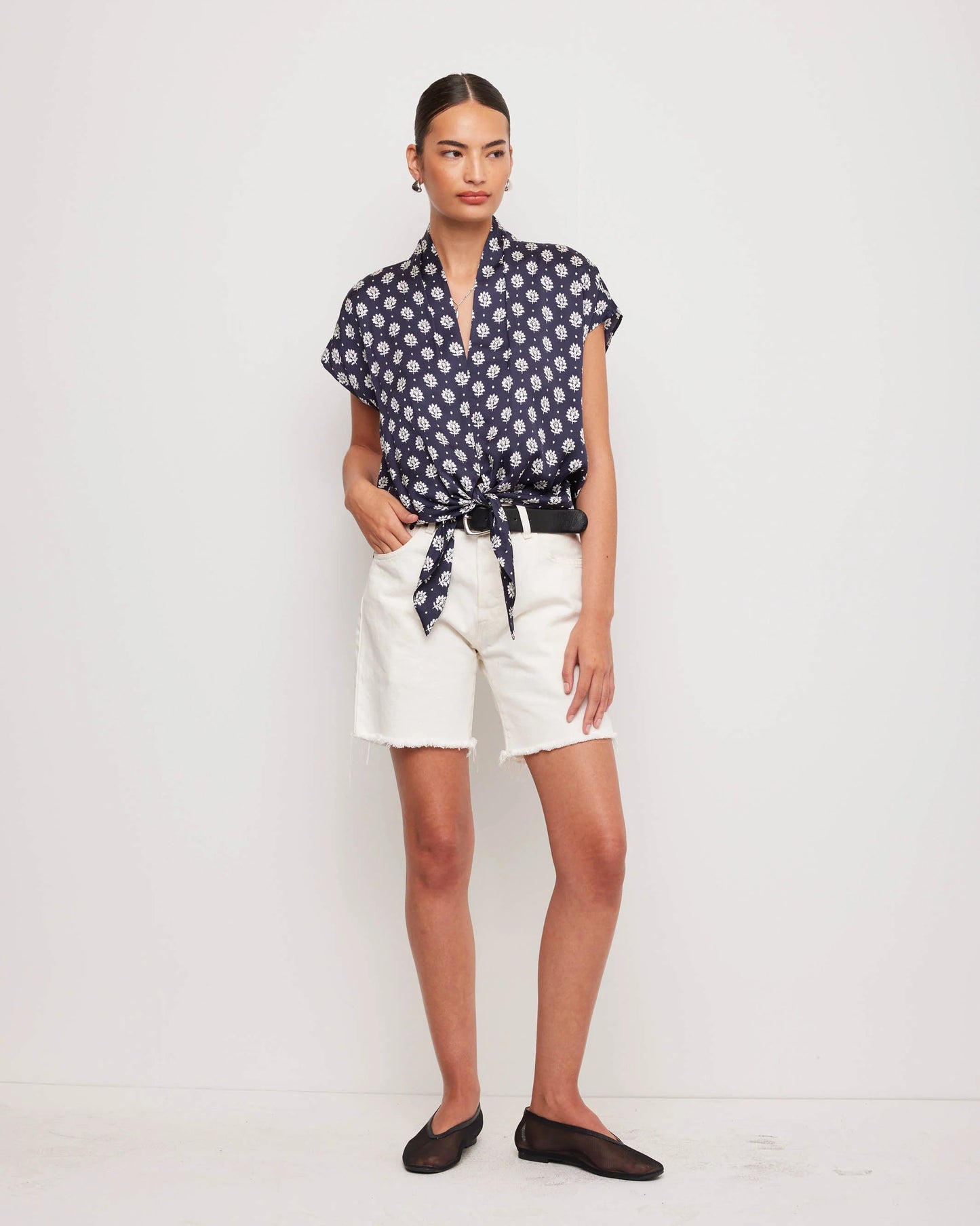 Woman wearing a patterned blouse and white shorts on a white background