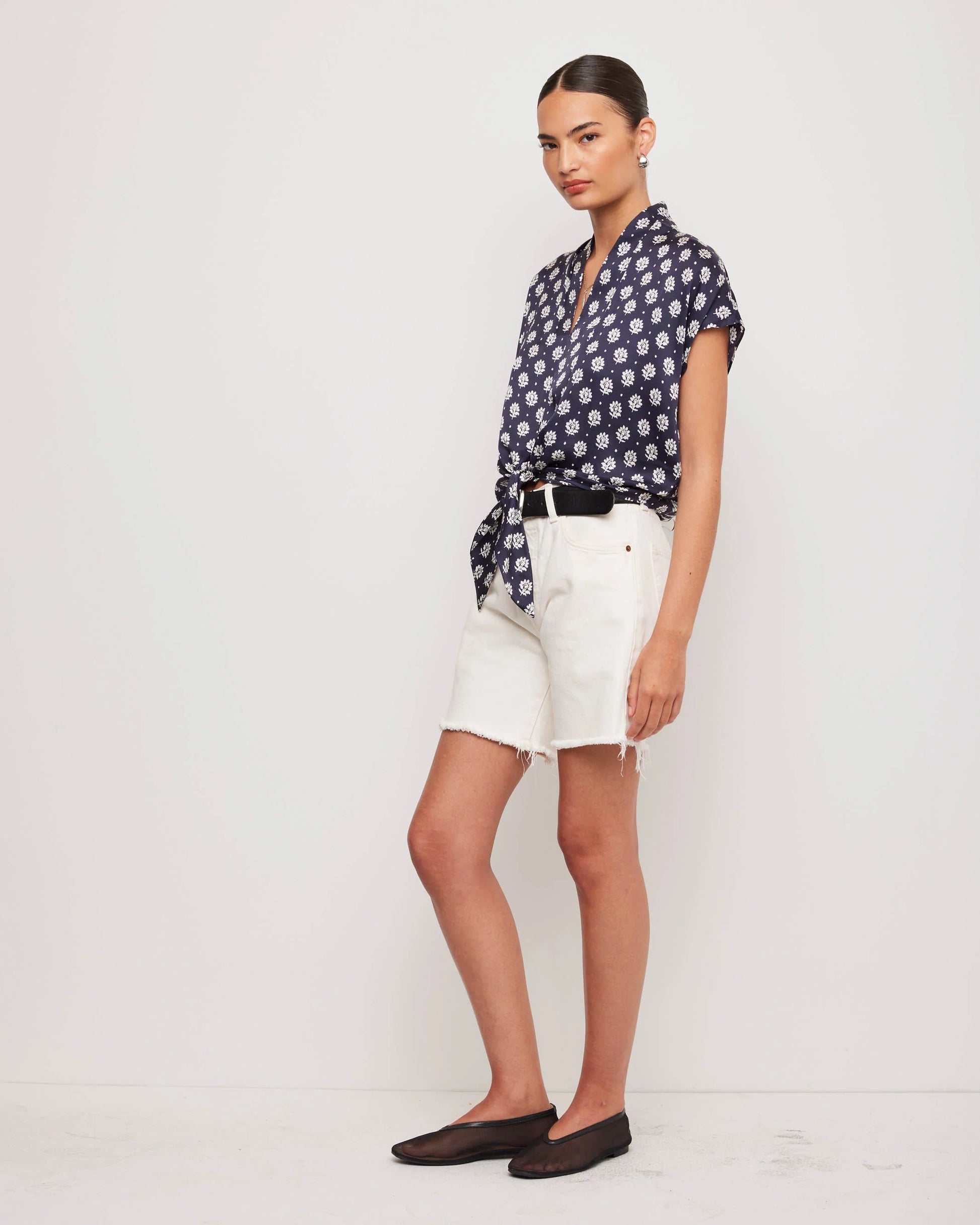 Woman wearing a navy floral blouse and white shorts on a light background