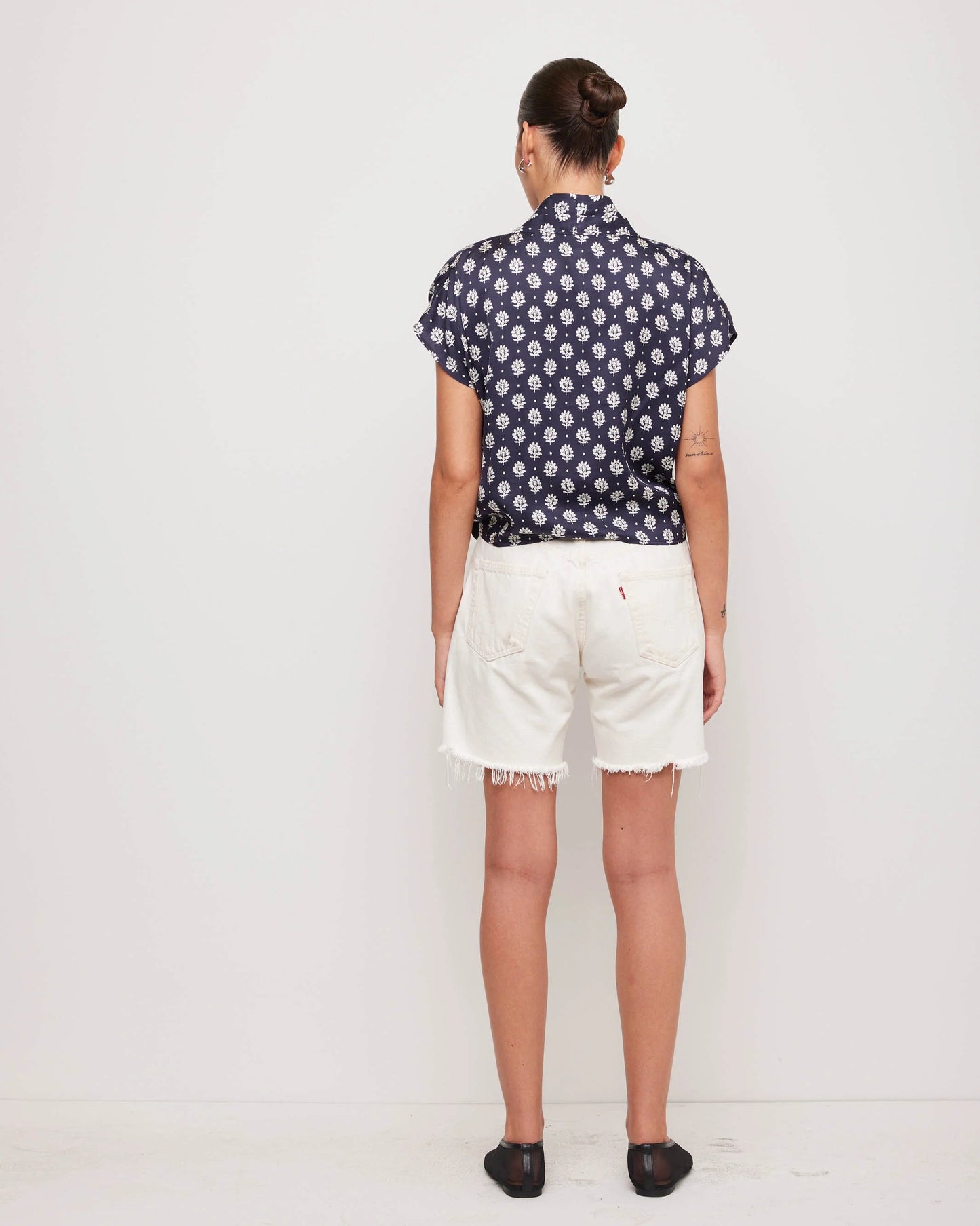 Person wearing a navy blue floral shirt and white shorts on a white background