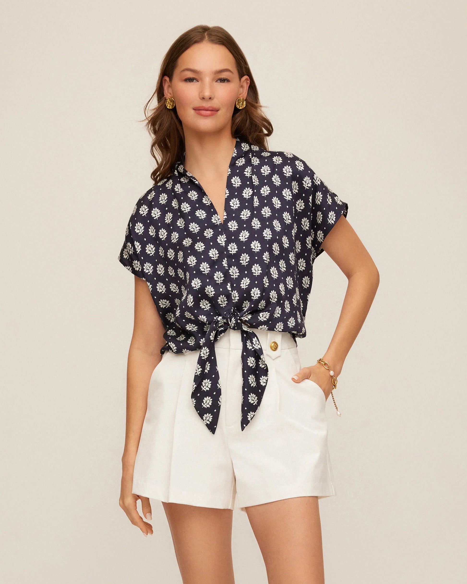 Woman wearing a navy floral shirt and white shorts on a beige background