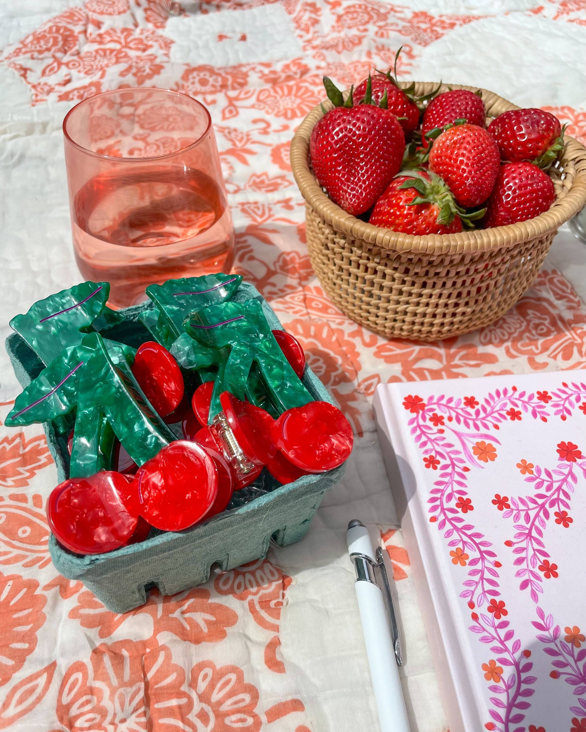 Cherry shaped hair clips in a small green basket resting on a patterned table cloth