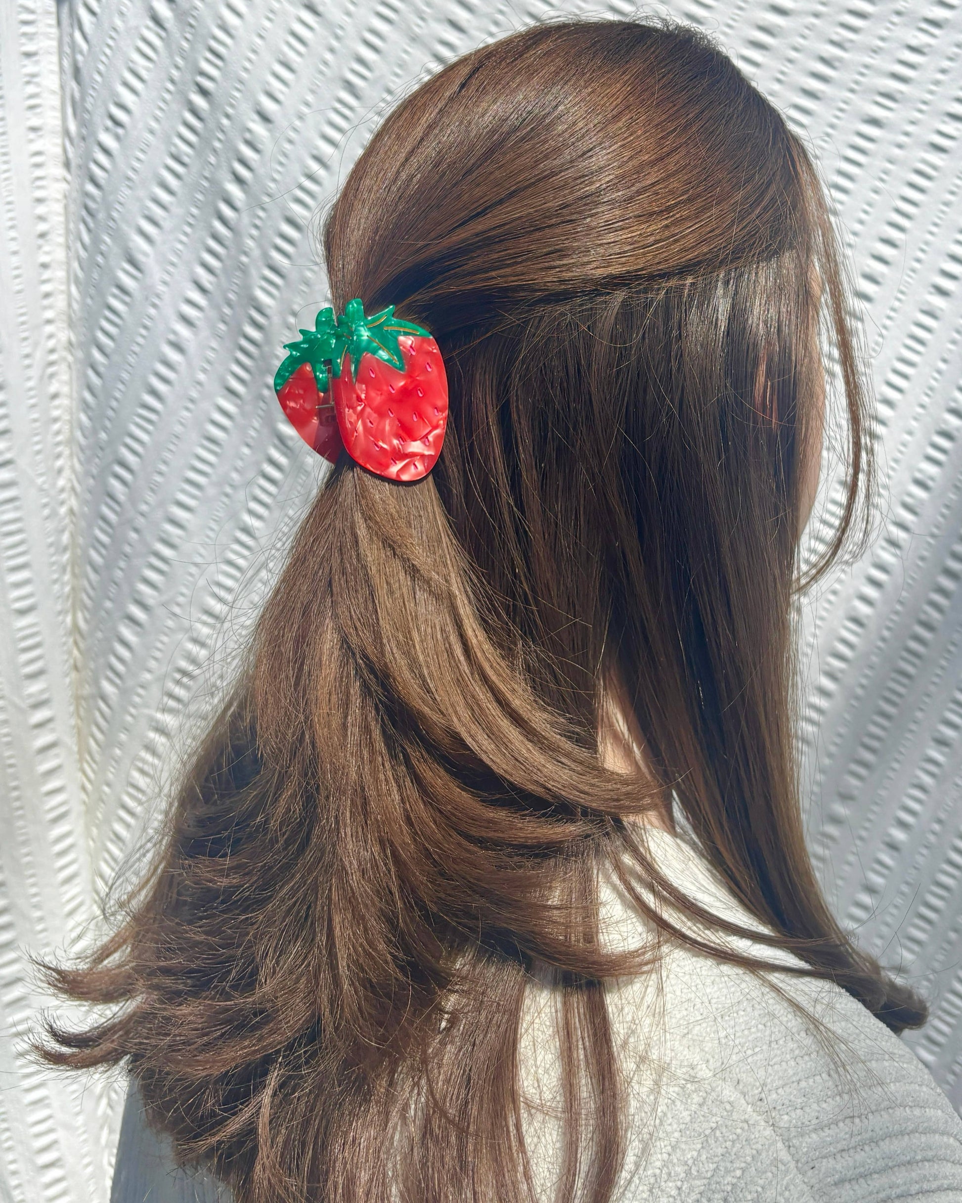 Hair tie shaped like a strawberry in a ponytail against a textured white background