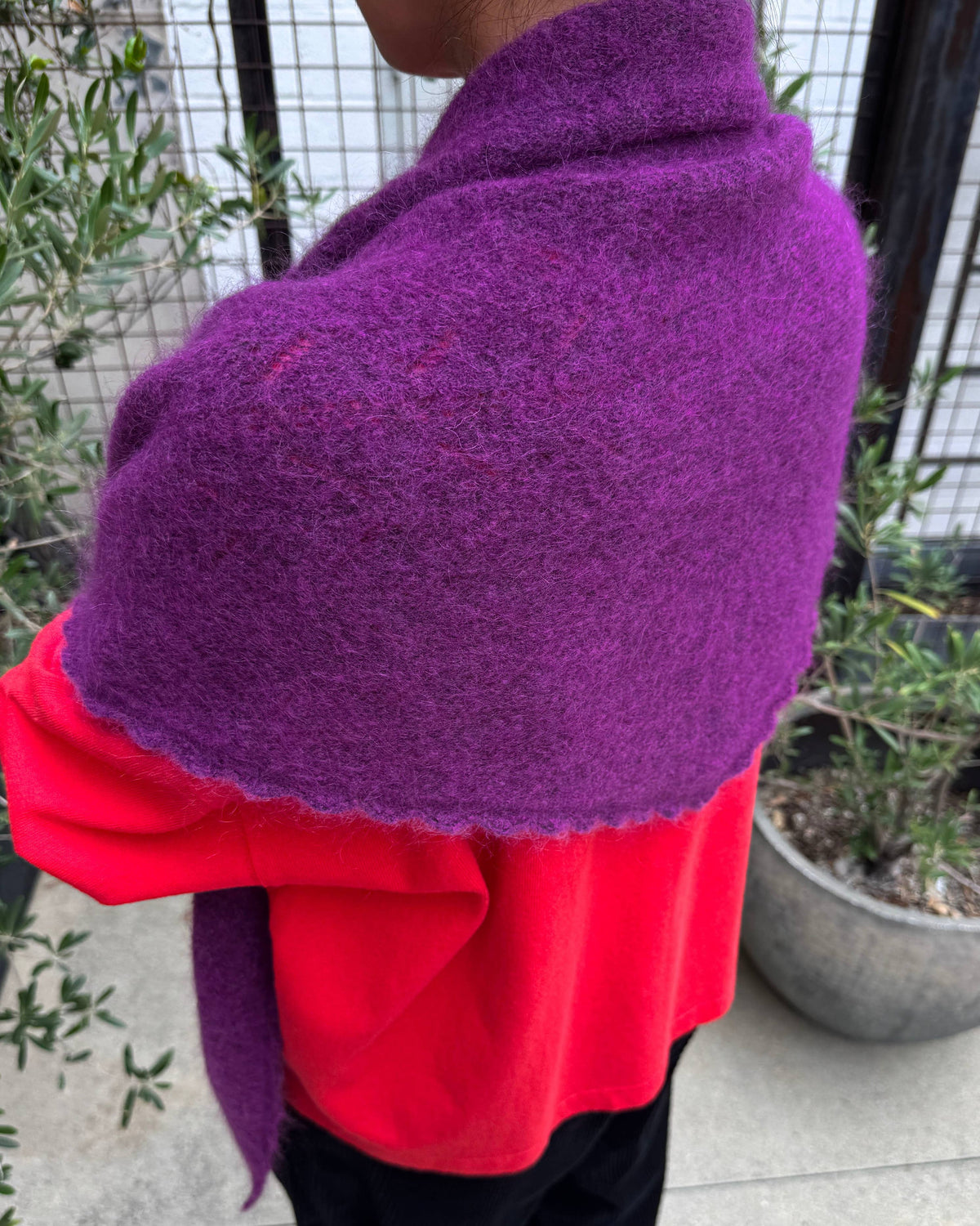 A person outdoors wearing a bright red top and black pants, with a thick fuzzy purple wrap or shawl draped over the shoulders.