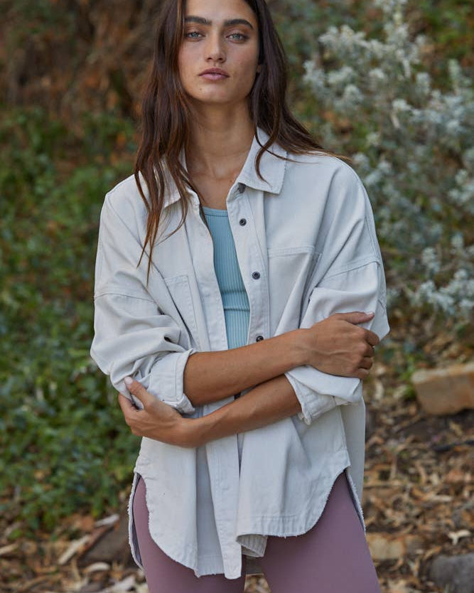 Woman standing outdoors in a natural setting wearing a light shirt and purple pants.