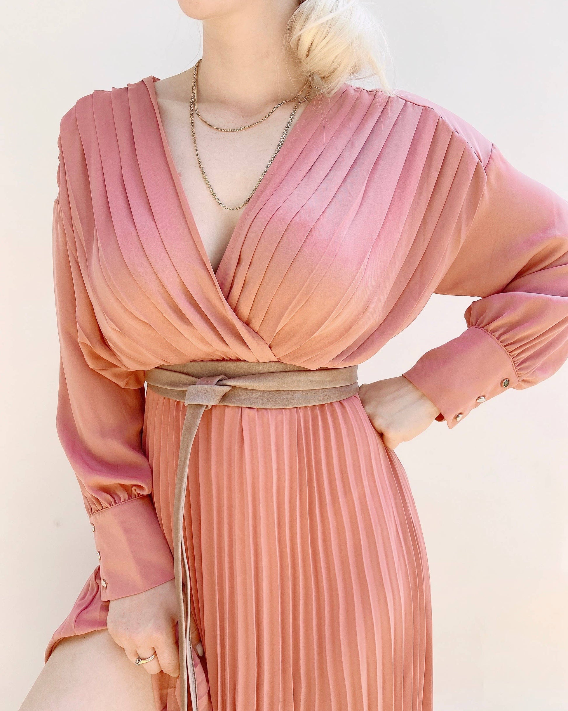 Woman wearing a pink pleated dress with a leather wrap belt on a white background