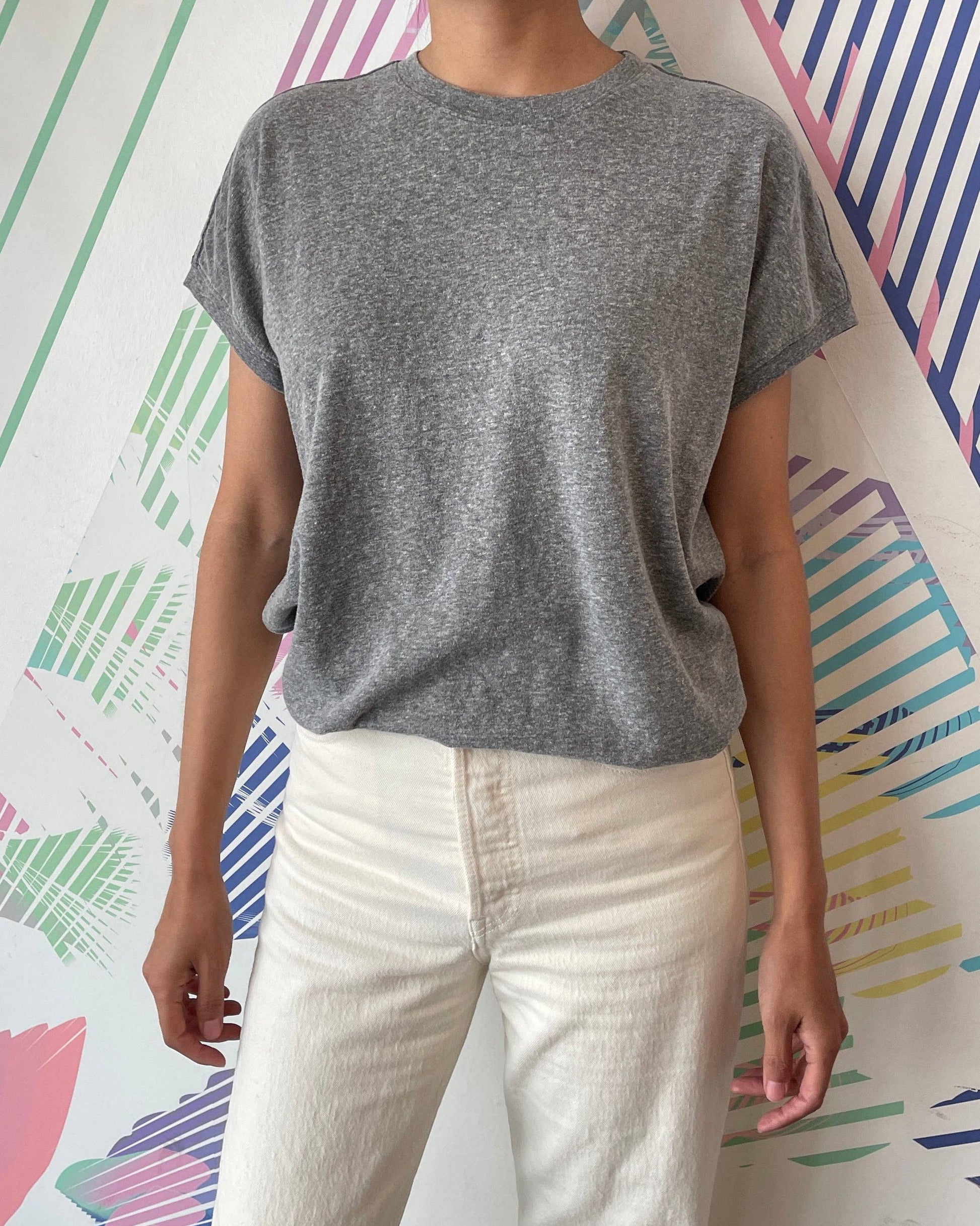Person wearing a gray t-shirt and white pants against a colorful abstract wall.