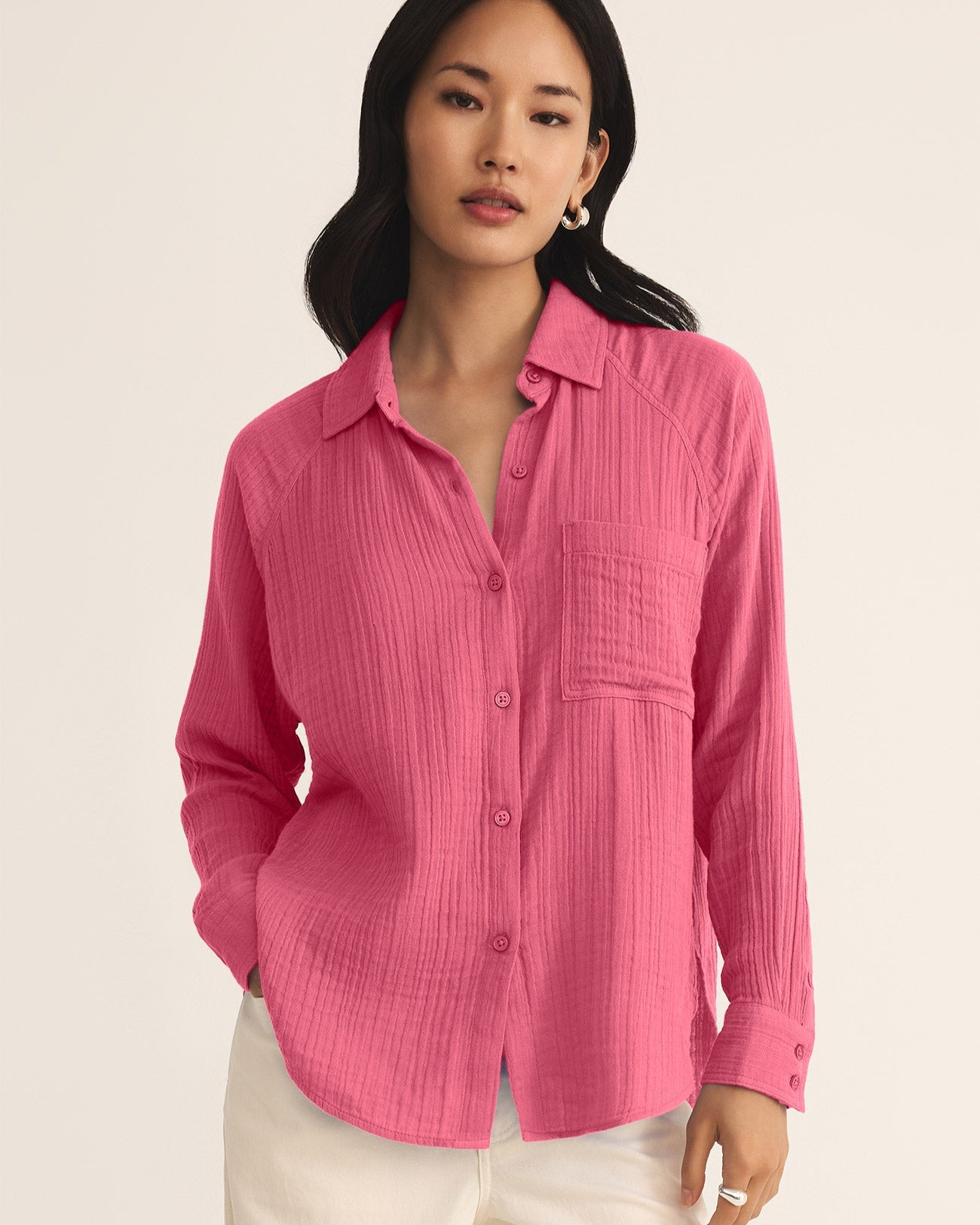 Woman wearing a pink button-up shirt and white pants on a beige background
