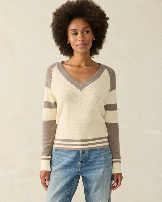 Model Wearing Faherty Throwback V Neck Sweater In Fenway wearing jeans on a beige background 