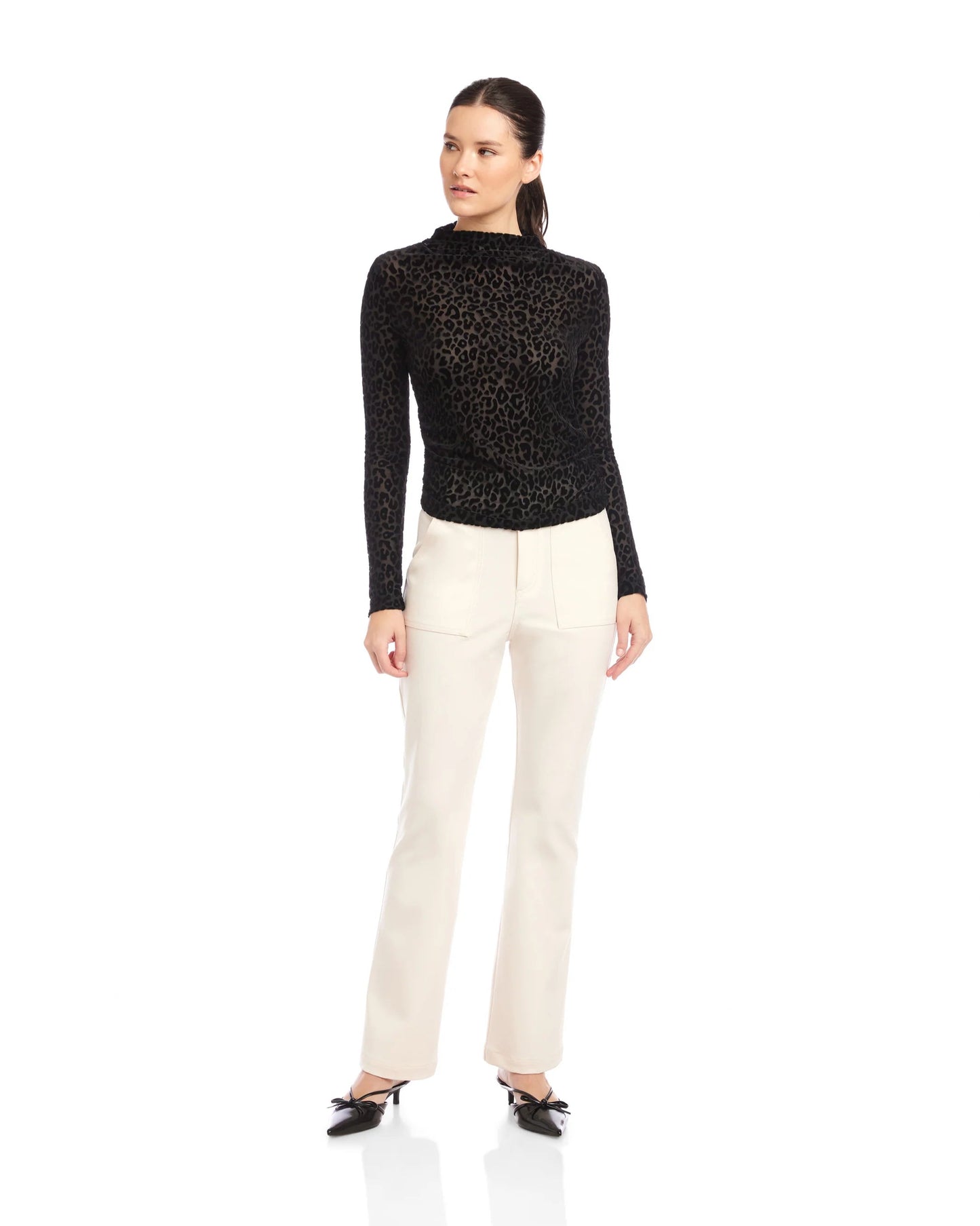 Woman wearing a black turtle neck top and white pants on a white background