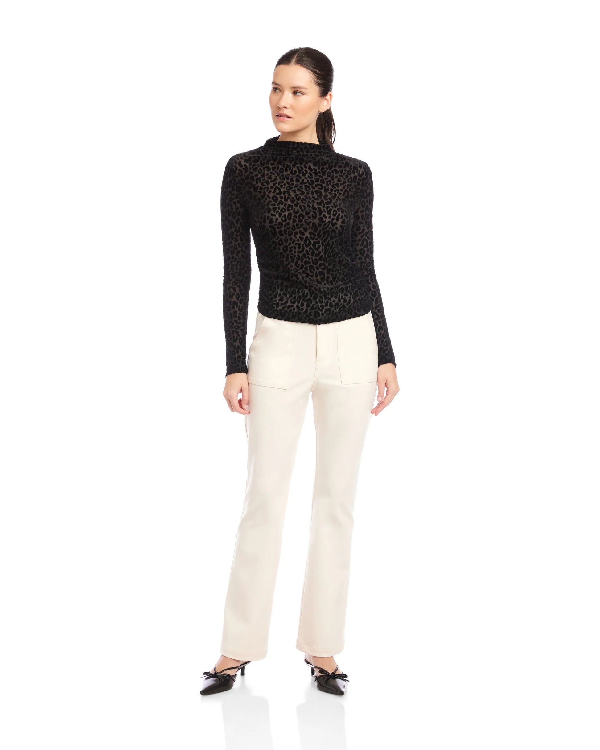 Woman wearing a black turtle neck top and white pants on a white background