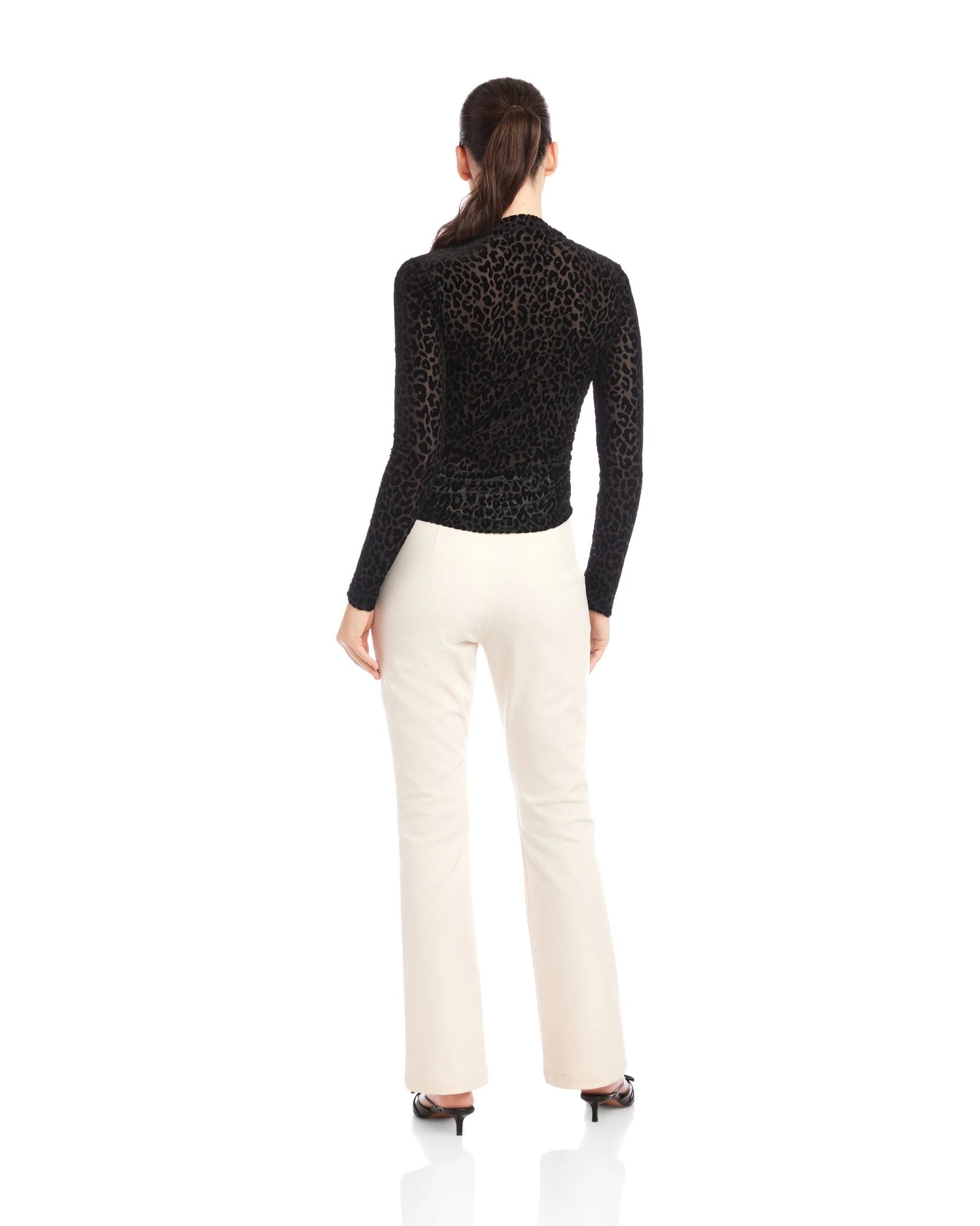 Woman wearing a black patterned top and white pants on a white background