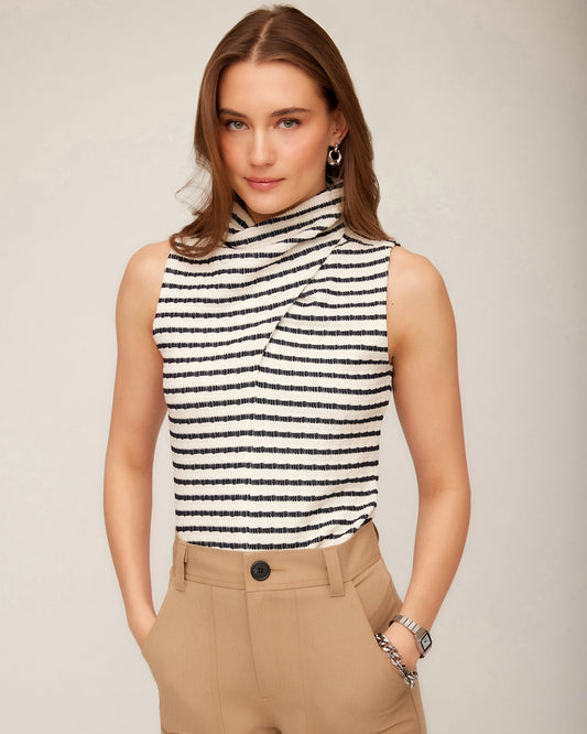 Model wearing the Abbey Turtleneck Tank with brown pants standing in front of a grey background