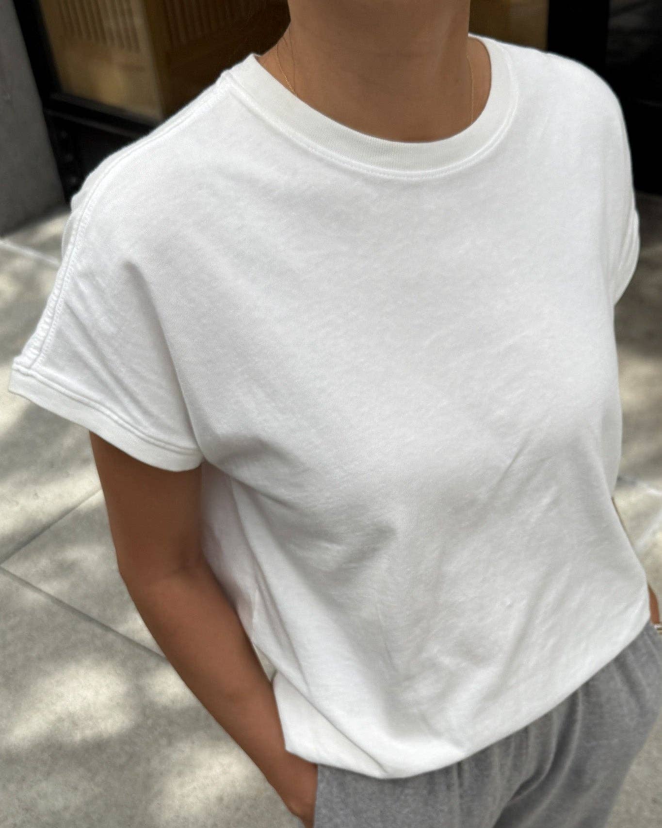 Person wearing a plain white t-shirt and gray pants on a sidewalk.