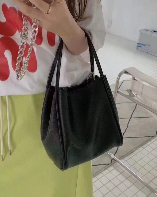 Person holding a black handbag with a white shirt and green pants in a bathroom setting
