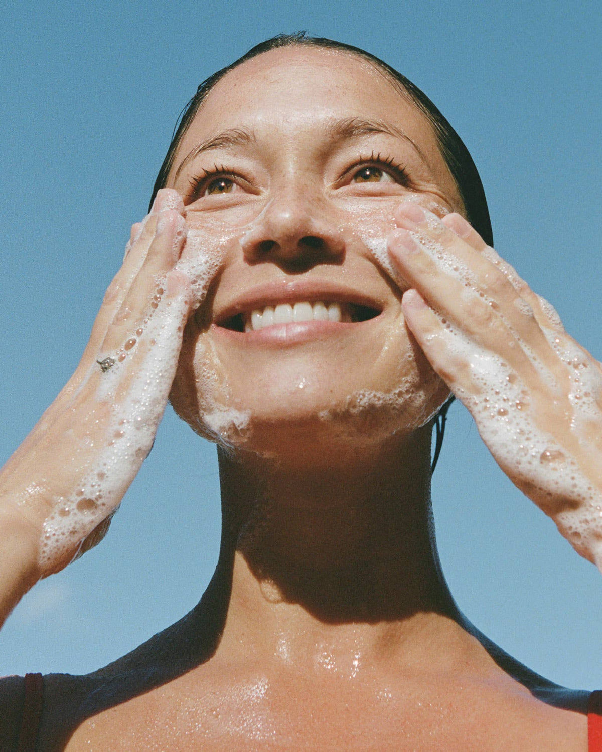 Woman washing her face with soap against a clear blue sky