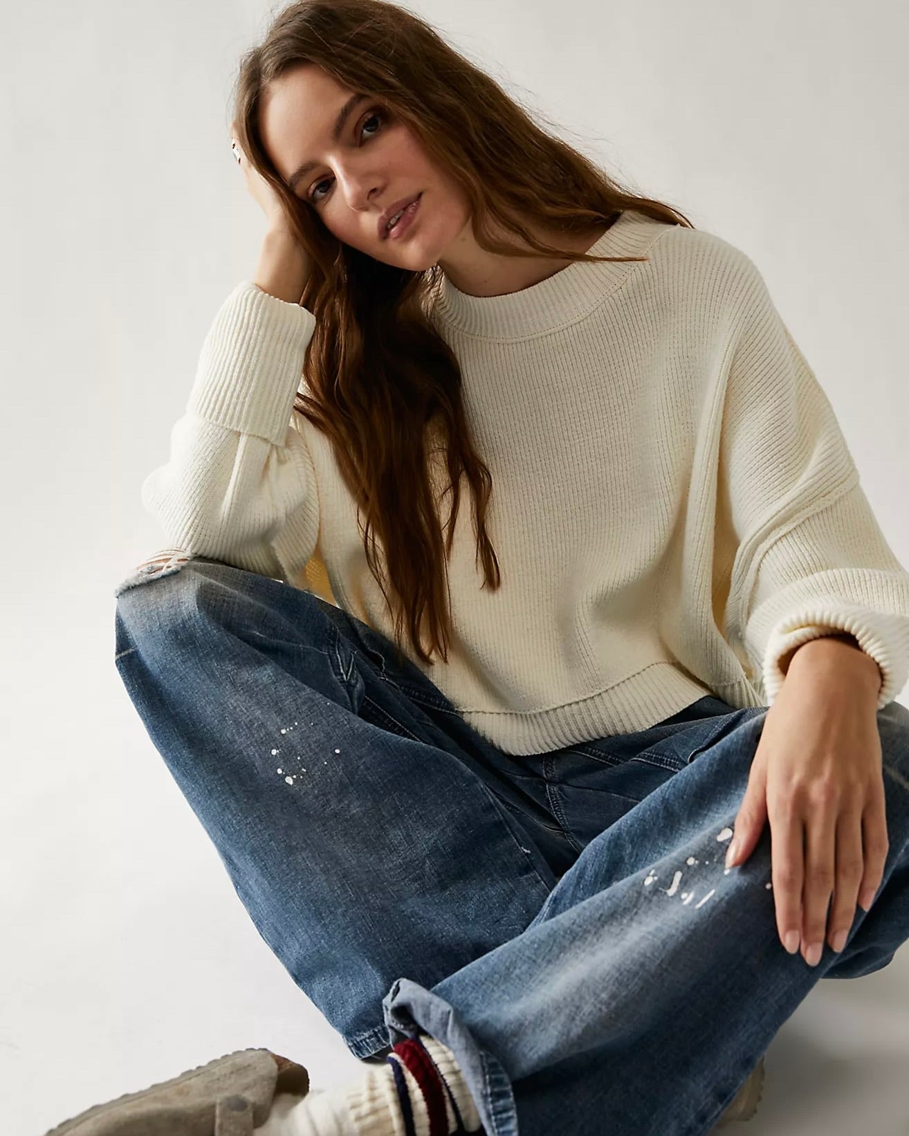 Model sitting cross legged wearing the Free People Easy Street crop pullover sweater and jeans against a white background.