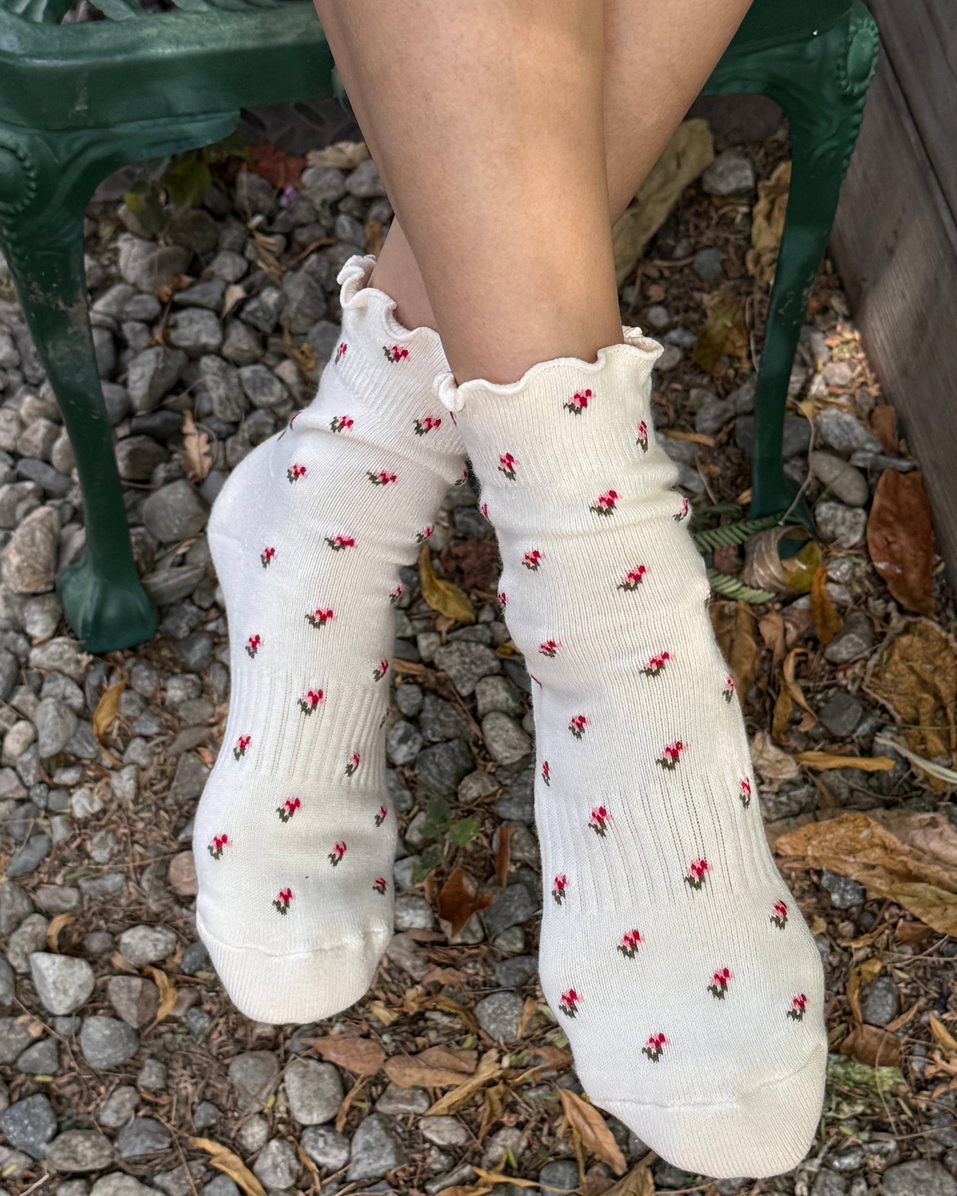 White socks with red floral patterns worn by a person sitting on a green bench.