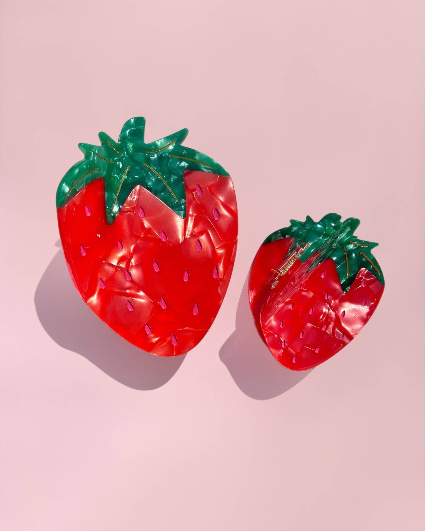Two strawberry-shaped hair clips on a pink background